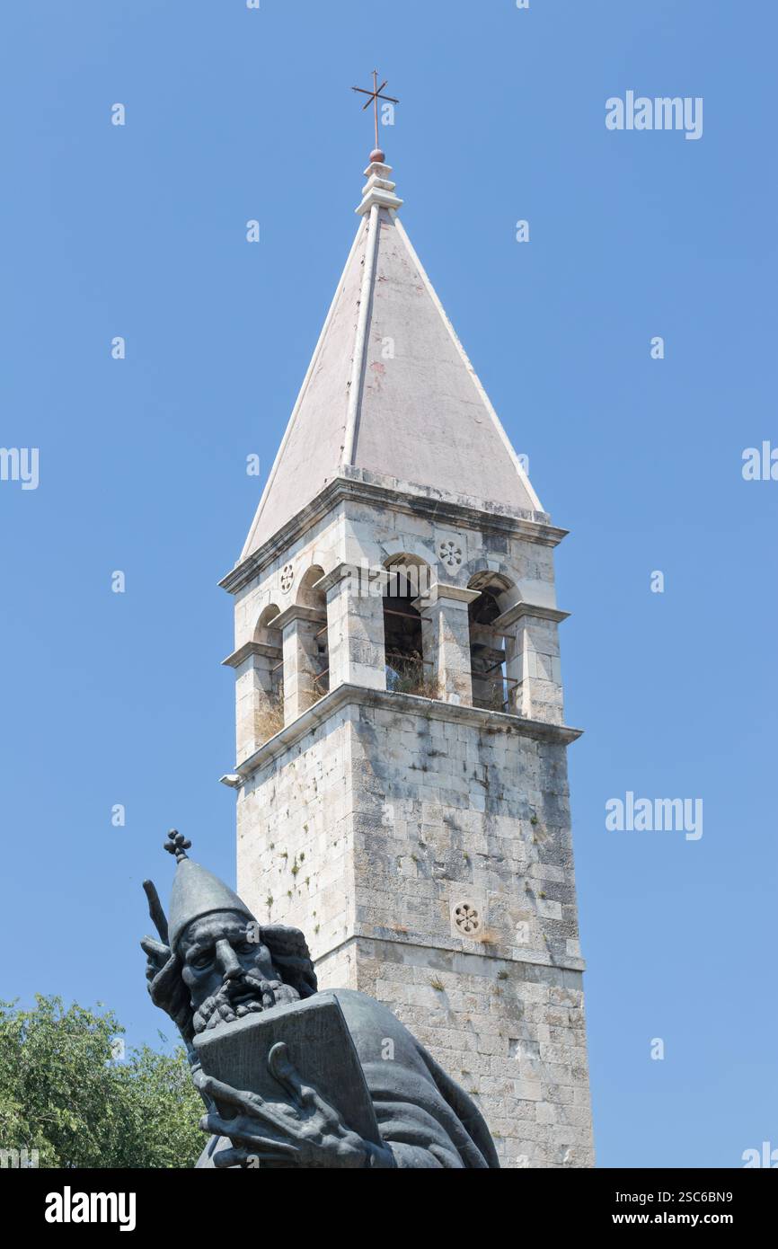 Eine ruhige Szene mit einem historischen Glockenturm neben einer hohen Statue, umgeben von üppigem Grün, unter einem klaren blauen Himmel, der an Kultur und Geschichte erinnert Stockfoto