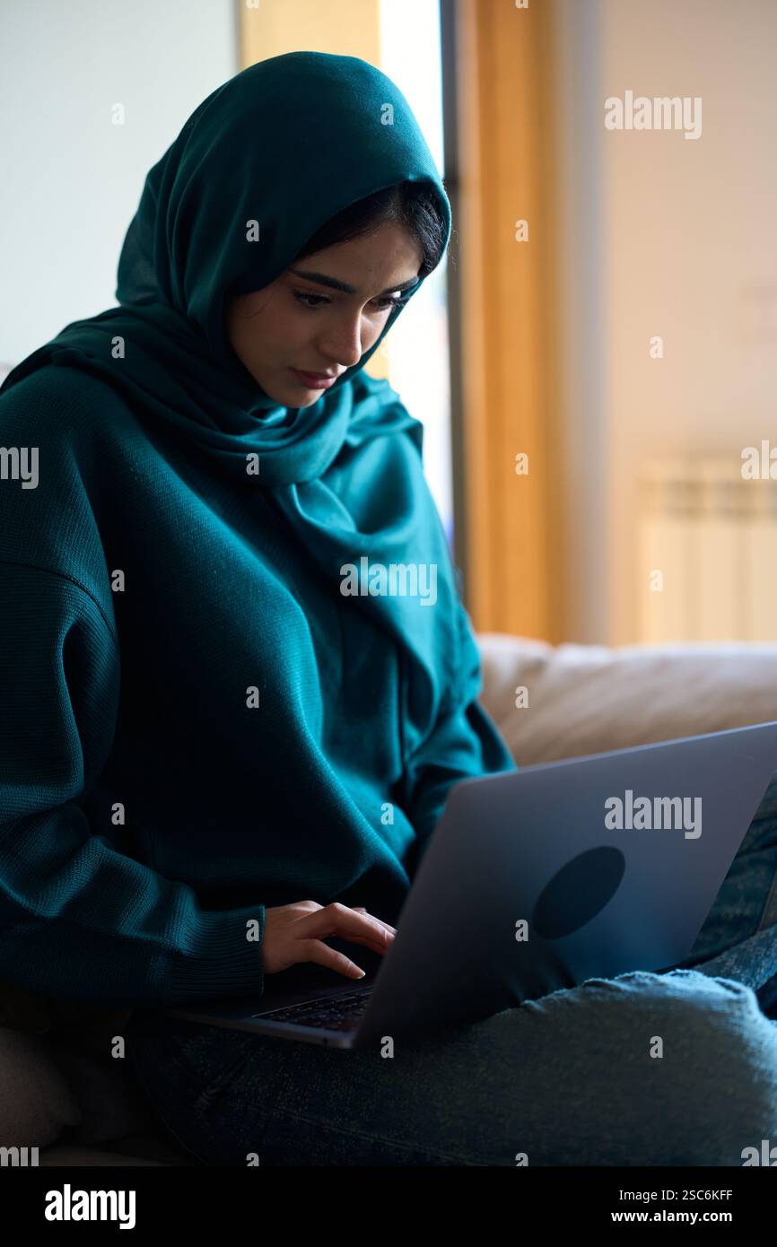 Eine junge muslimische Frau im Hijab, die von zu Hause aus auf einem Laptop arbeitet Stockfoto