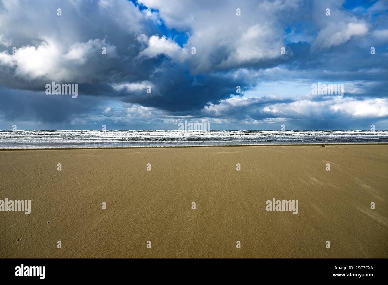 Ein riesiger Sandstrand unter einem dramatisch bewölkten Himmel, mit Wellen, die in der Ferne zusammenbrechen. Stockfoto