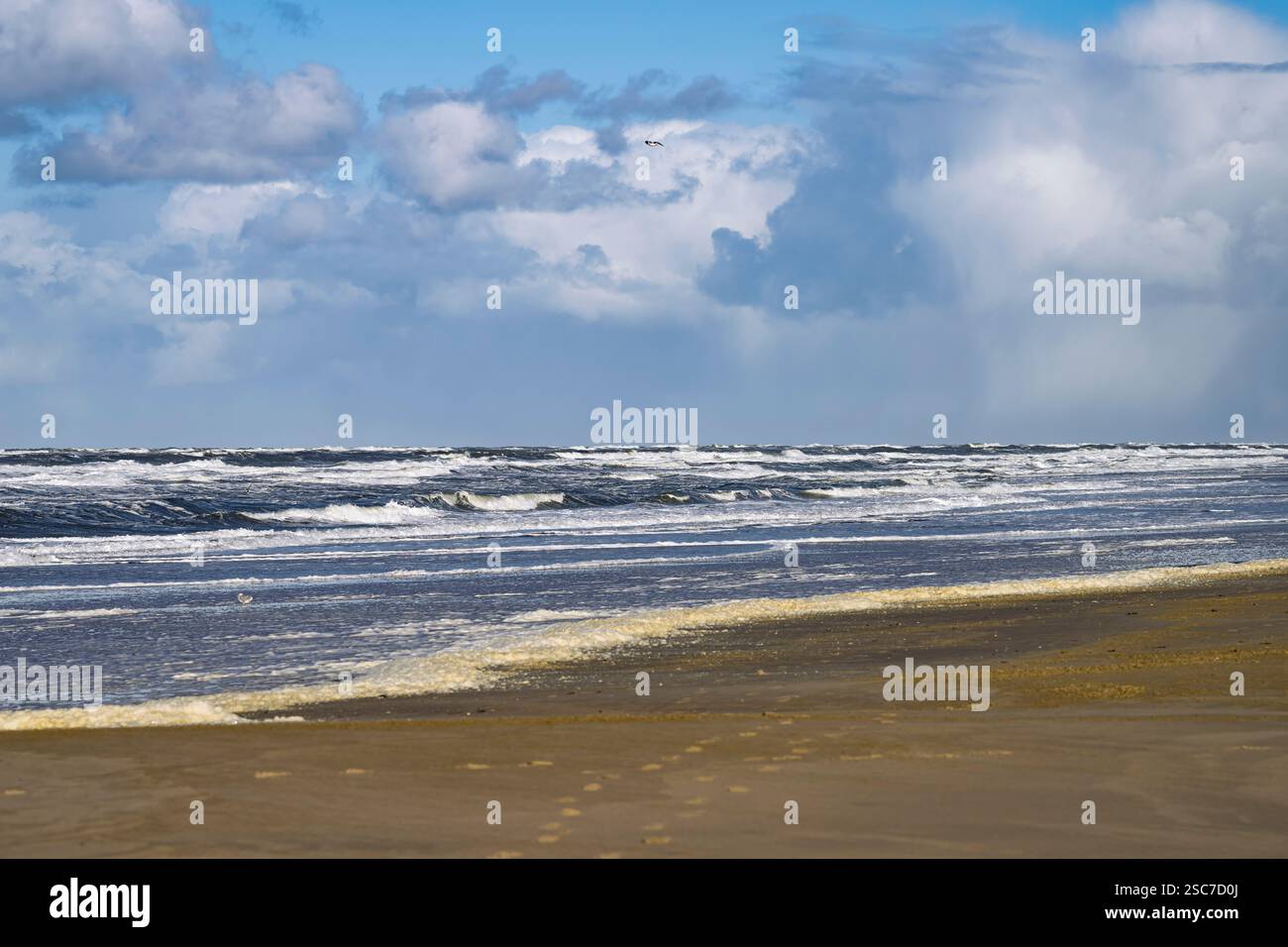 Eine ruhige Strandszene mit sanften Wellen, die unter teilweise bewölktem Himmel gegen das Ufer schlagen. Stockfoto