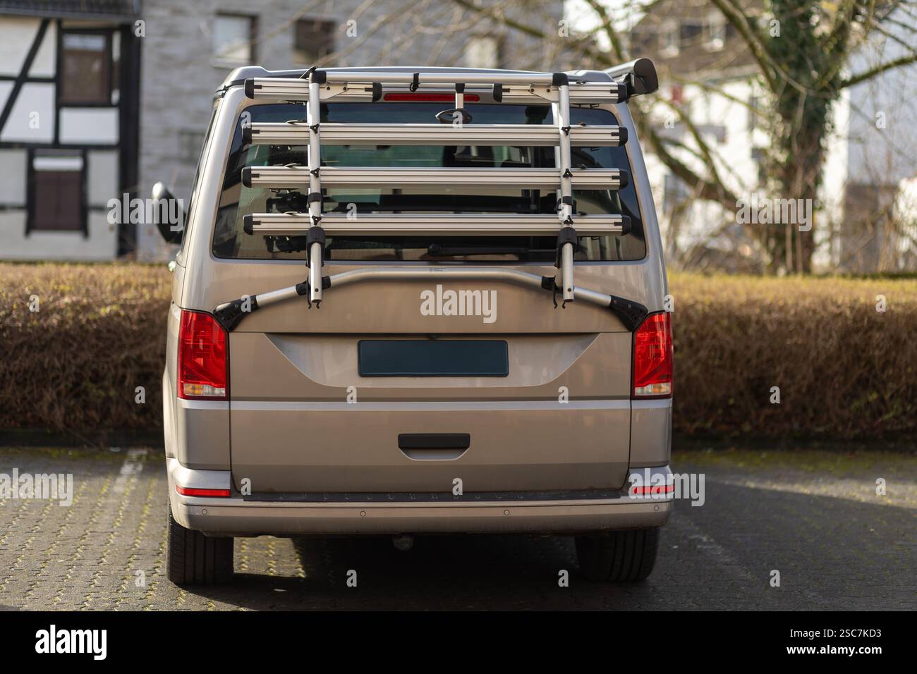 Ein silberner Van parkt in einer ruhigen Nachbarschaft mit einem Fahrradträger, der hinten befestigt ist. Die Umgebung umfasst eine Reihe von Häusern und Bäumen, alle darunter Stockfoto