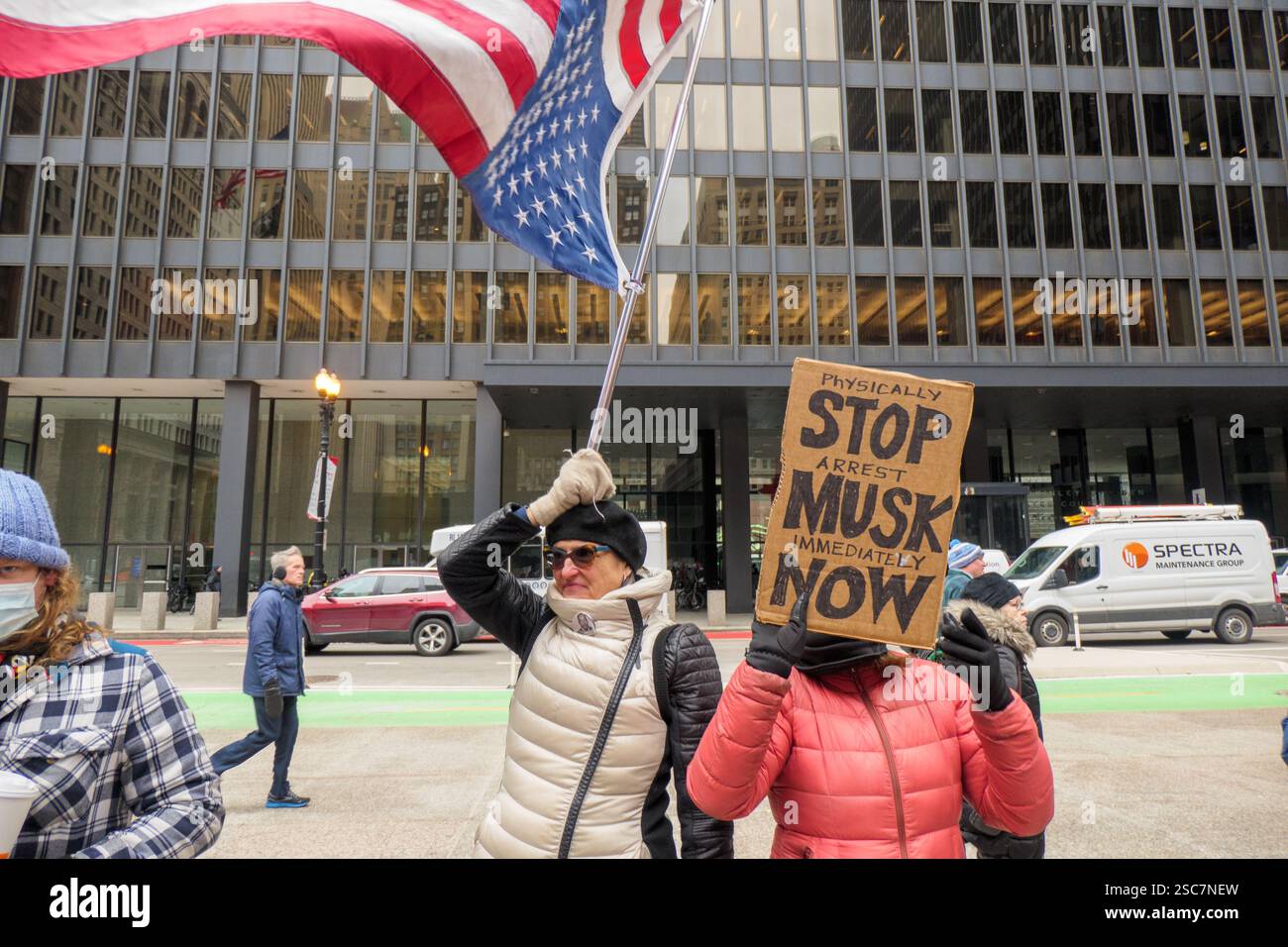 Eine Frau hält eine umgedrehte amerikanische Flagge, während eine andere einen Anti-Elon Musk-Seufzer gegen Donald Trump und Elon Musk, Federal Plaza, Chicago, Illinois, hält. Stockfoto