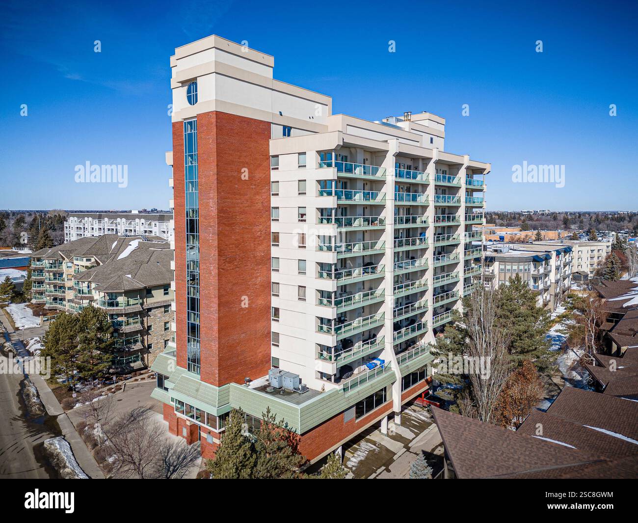 Großes Backsteingebäude mit grünem Dach und Balkon. Das Gebäude ist von Bäumen und Häusern umgeben Stockfoto