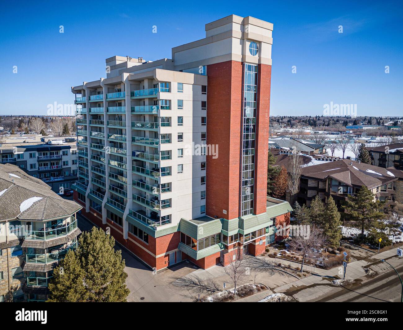 Großes rotes Gebäude mit weißer Fassade. Das Gebäude ist von Bäumen und Häusern umgeben. Der Himmel ist klar und blau Stockfoto