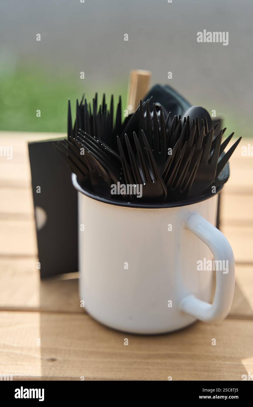 Eine Sammlung von Gabeln und verschiedenen Besteck, die in einem weißen Becher auf einem Tisch angeordnet sind Stockfoto