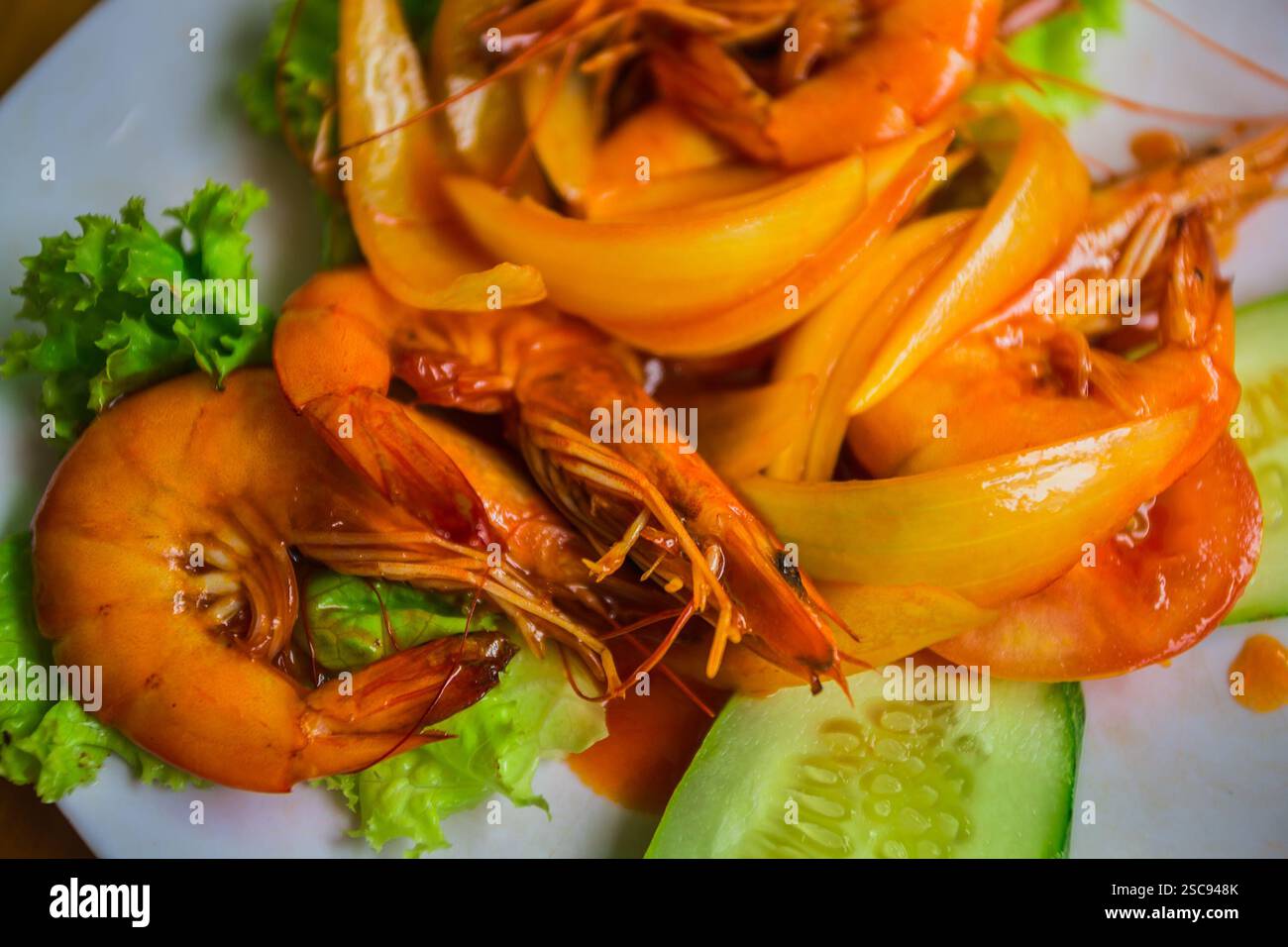 Garnelen mit Zwiebeln, Salat, Gurke und Sauersauce auf einem weißen Teller Stockfoto
