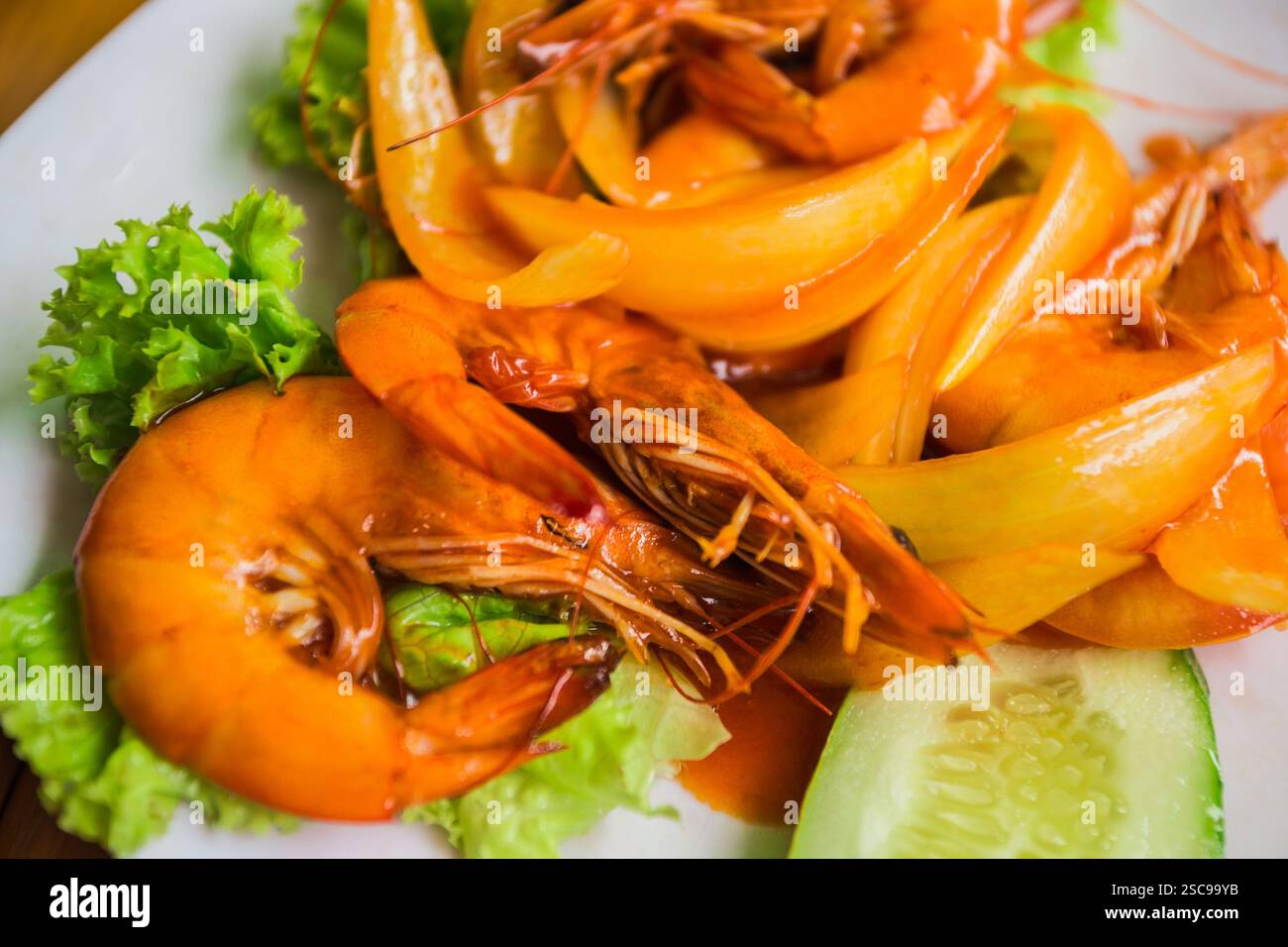 Garnelen mit Zwiebeln, Salat, Gurke und Sauersauce auf einem weißen Teller Stockfoto