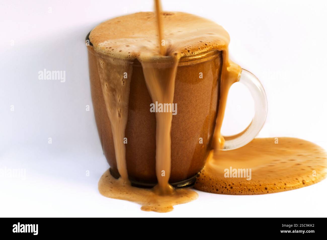 Heißes, schaumiges Schokoladengetränk in Glasbecher. Getränk überläuft auf Becher und auf hellem Hintergrund, Nahaufnahme. Stockfoto