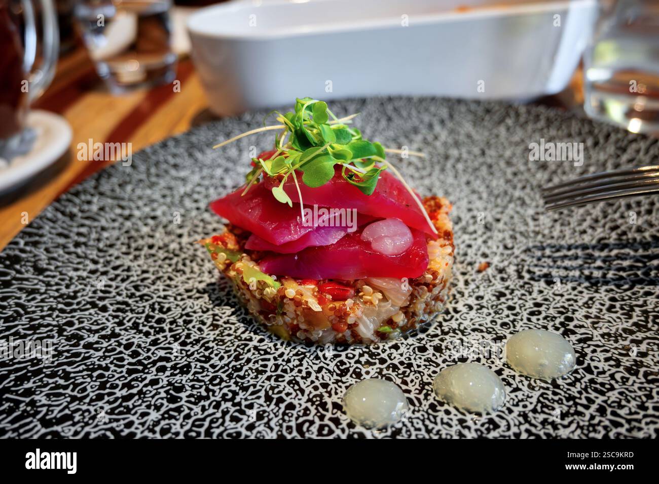 Teller mit Vorspeise aus marinierter Bachforelle auf Quinoa, Linsen, Zwiebeln und Mango, Restauranttisch. Stockfoto