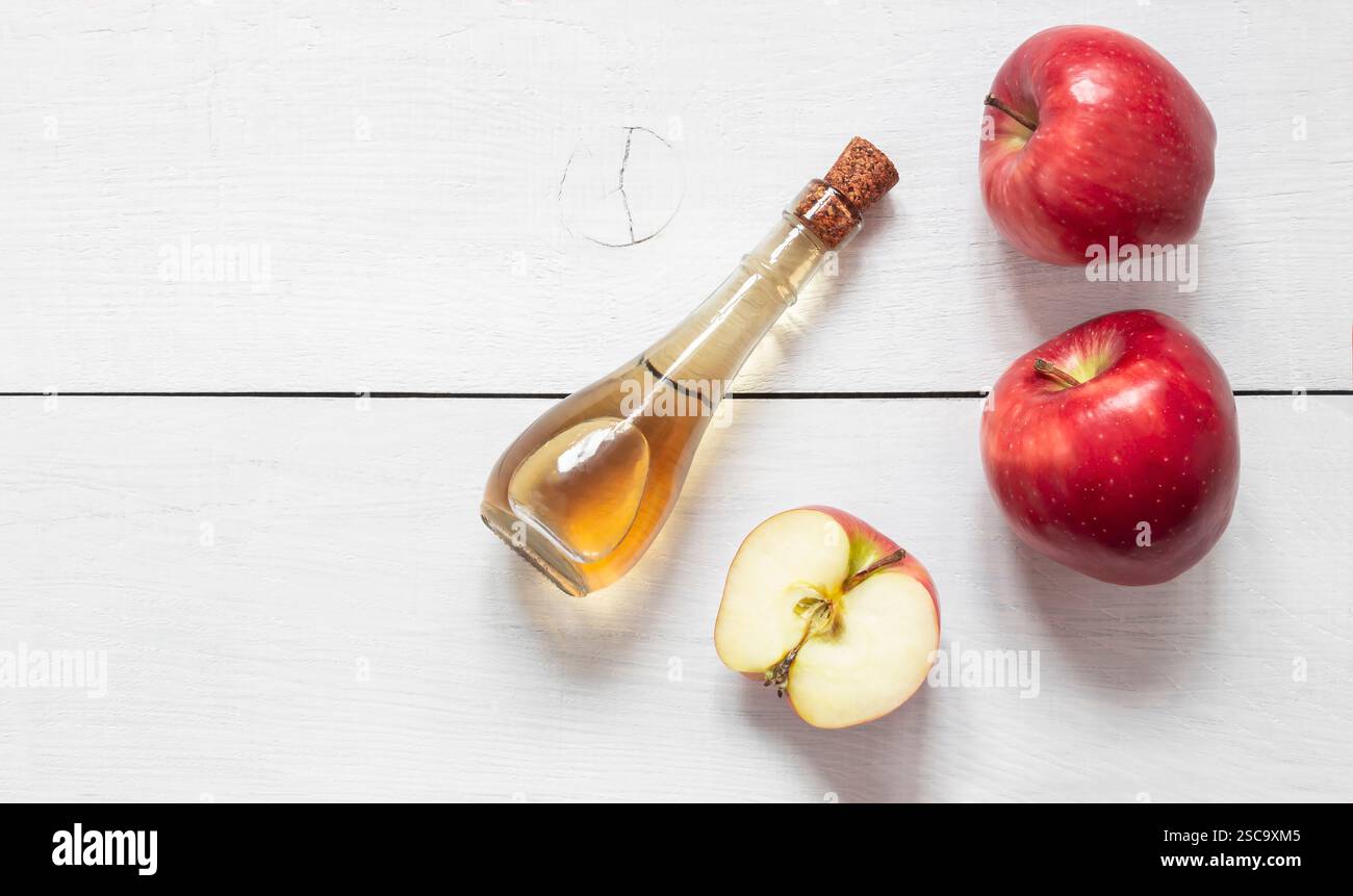 Glasflasche mit Bio-Apfelessig mit Reifen frischen roten Äpfeln auf hölzernem Hintergrund, selektiver Fokus, Platz für Text Stockfoto