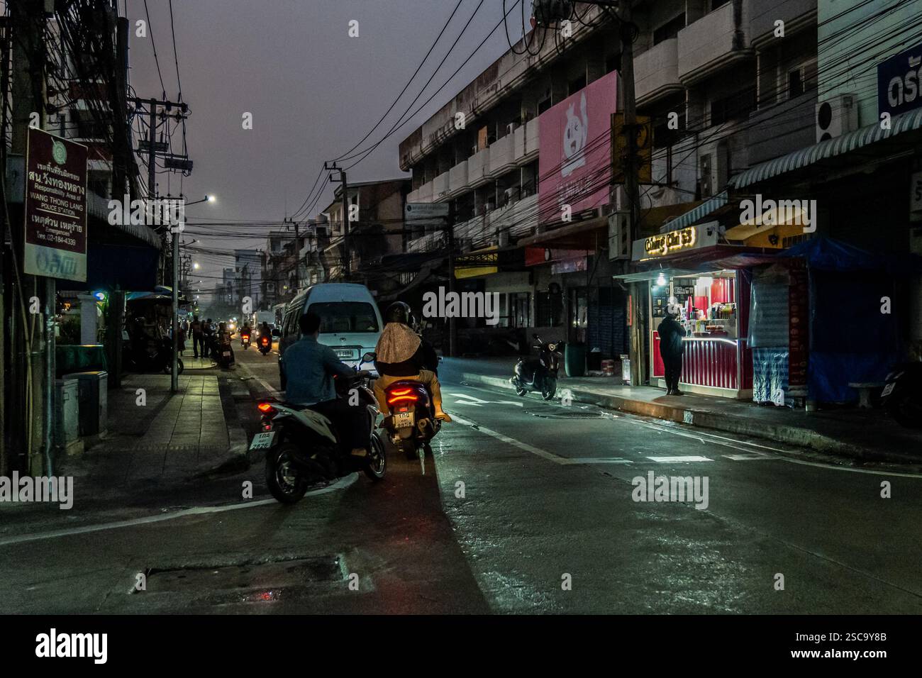 Bangkok, Thailand. Februar 2025. Ein Blick auf eine Straße bei Sonnenaufgang, wo Pendler auf Motorrädern und Autos durch den dicken Smog navigieren. Ein Café ist bereits geöffnet, während die Menschen vor Staus aufbrechen. Bei Sonnenaufgang laufen und joggen die Menschen durch die trüben Straßen, trotz schlechter Luftqualität aufgrund der hohen Luftverschmutzung, die die kühlere Luft optimal nutzt, bevor die Hitze des Tages einsetzt. Pendler auf Motorrädern und Autos navigieren durch den dichten Smog, bevor der Stau beginnt. Quelle: SOPA Images Limited/Alamy Live News Stockfoto