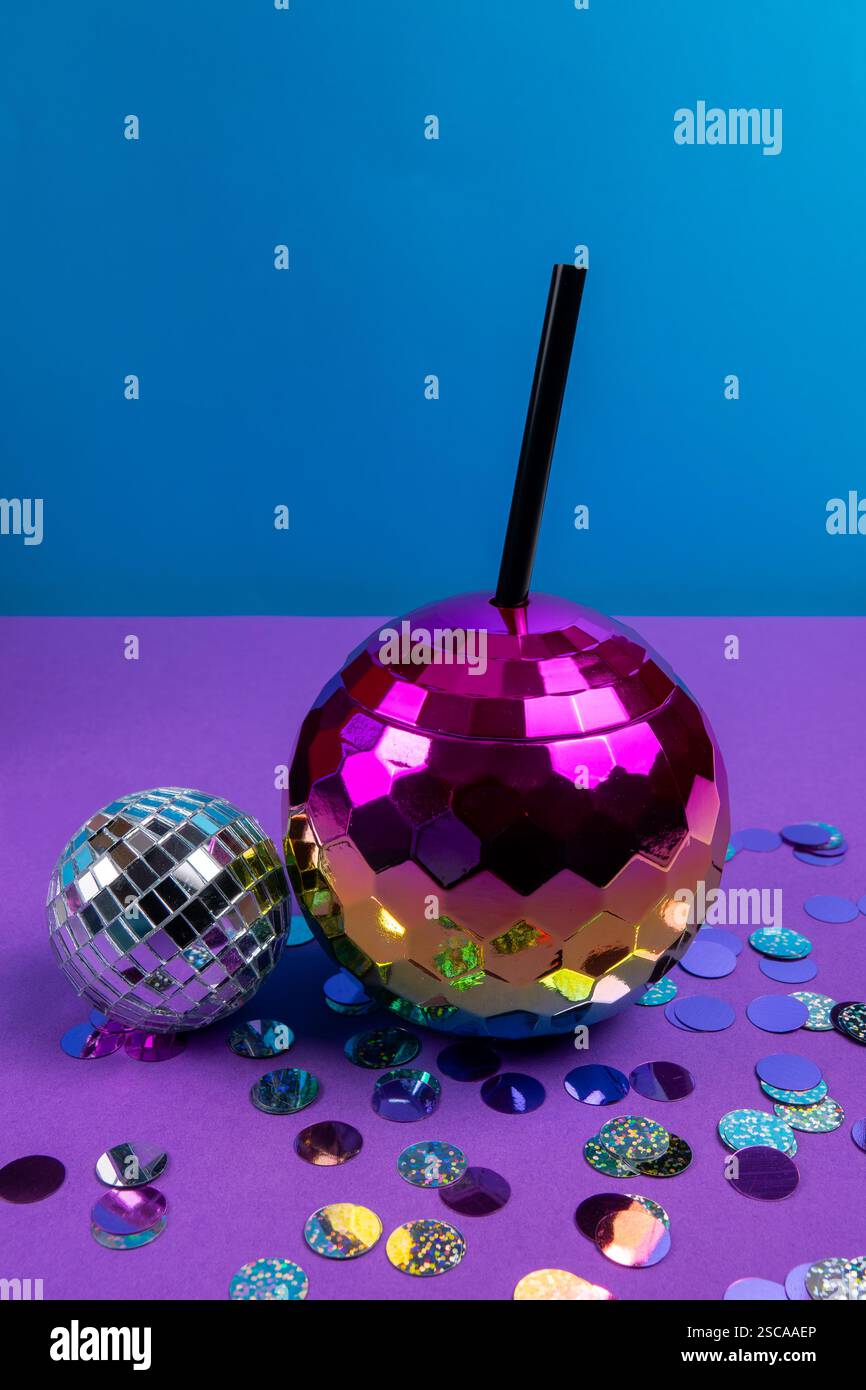 Eine große rosafarbene Discokugel und eine kleinere silberne Discokugel ruhen auf einer farbenfrohen, violetten Oberfläche, die mit glänzendem Konfetti verstreut ist, was eine Partystimmung andeutet. Stockfoto