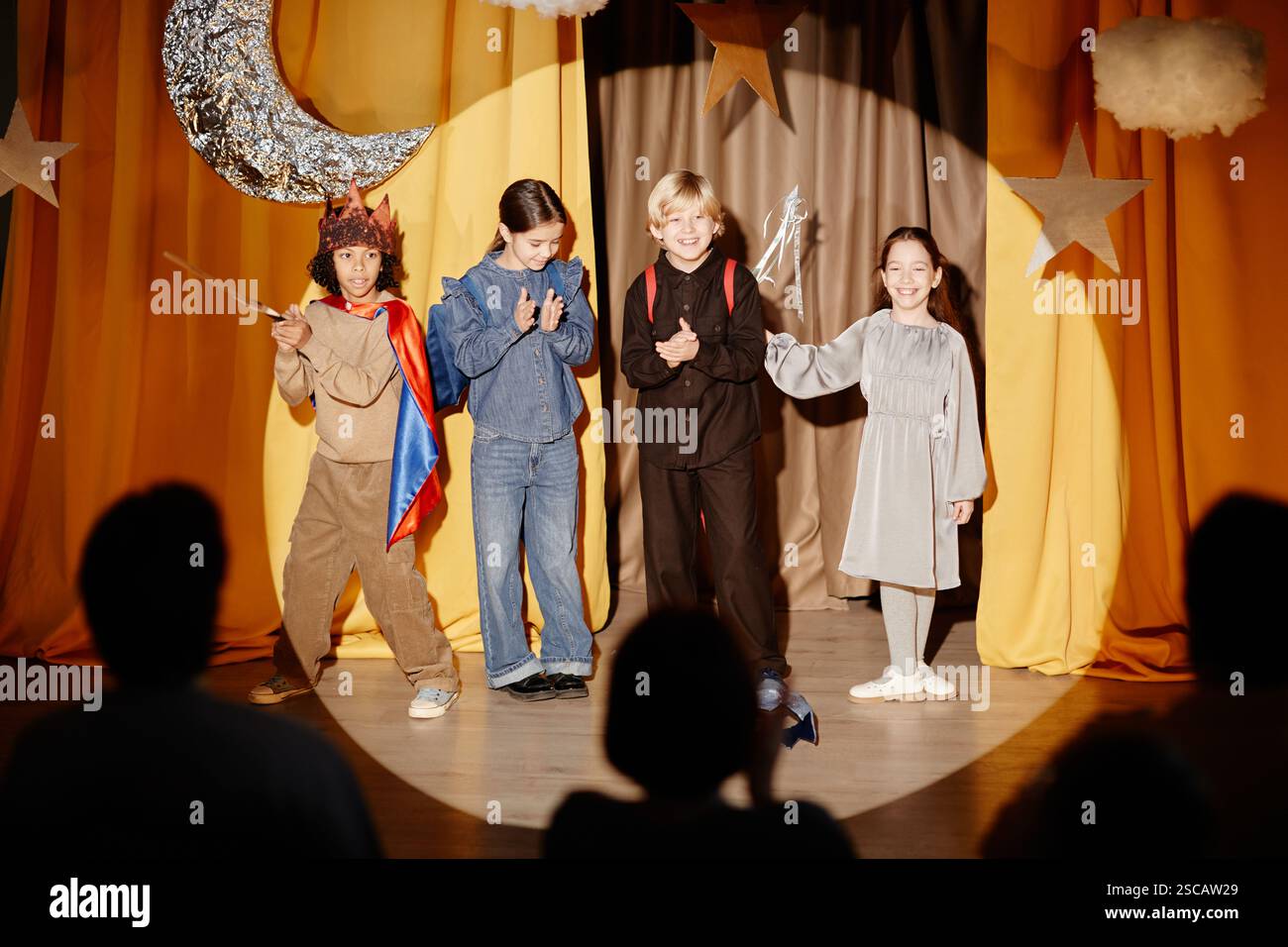 Eine Gruppe von Kindern in Kostümen, die auf der Bühne mit hellgelben Vorhängen im Hintergrund ein Theaterstück mit Sternen und Mond-Requisiten spielen Stockfoto