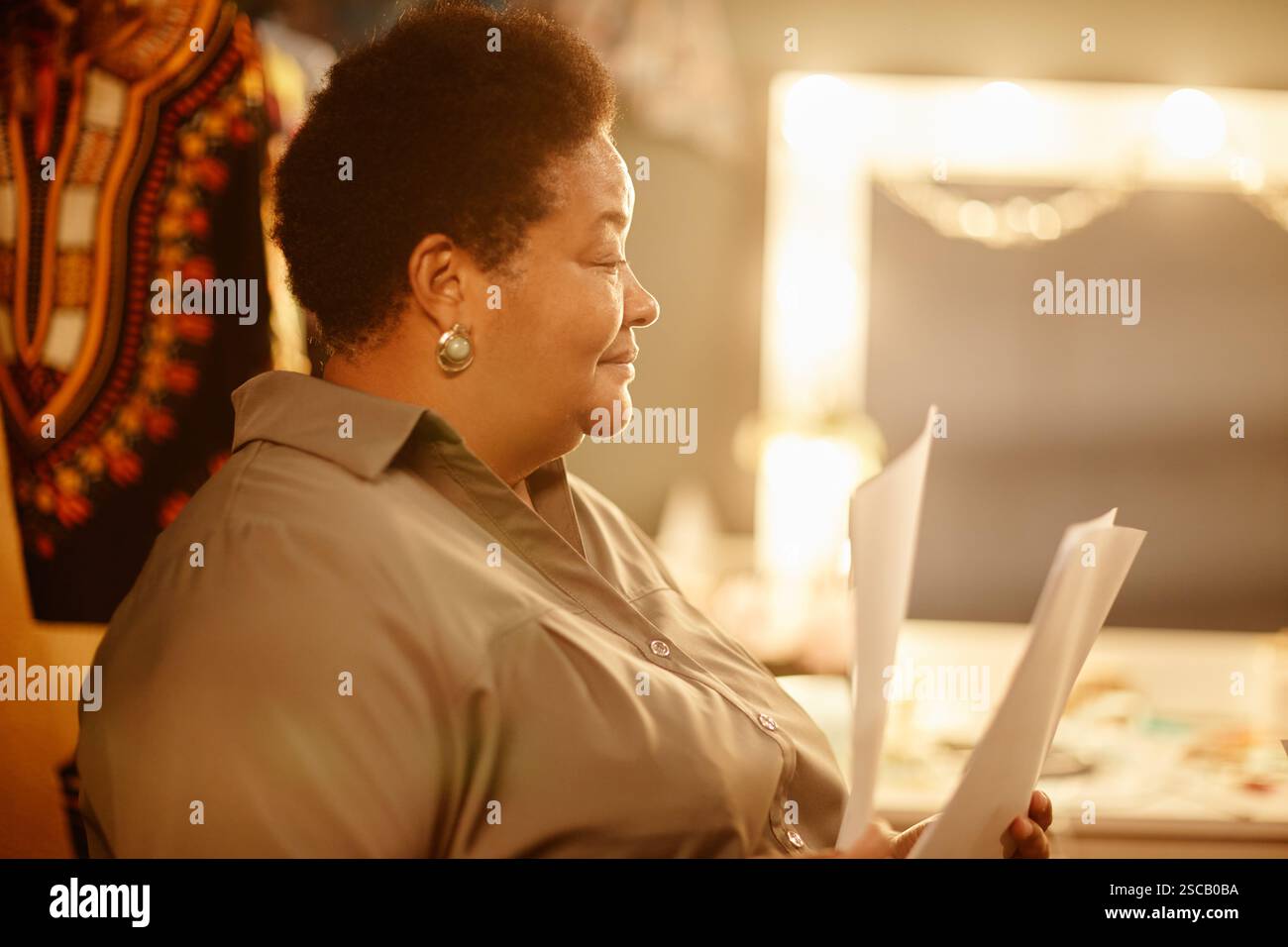 Frau, die Dokumente in einem sanft beleuchteten künstlerischen Atelier hält und liest, wirkt fokussiert und reflektierend Stockfoto