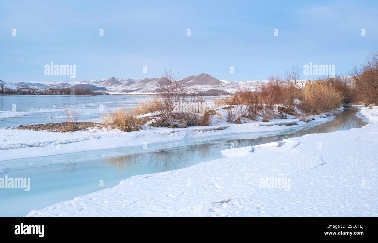 Der Fluss Ili mit türkisfarbenem Wasser in Almaty, Kasachstan, fließt im Winter zwischen schneebedeckten Bergen und eiskalten Küsten. Stockfoto