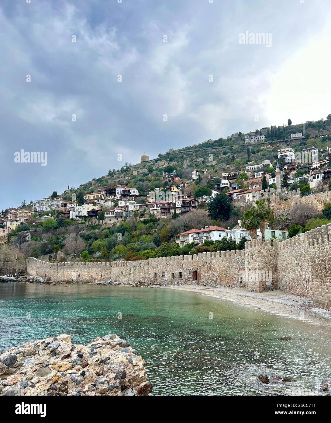 Wunderschönes Foto von Häusern auf einem Hügel und einer Burgmauer neben dem klaren Wasser des Mittelmeers - Smartphone-aufgenommenes Stockfoto