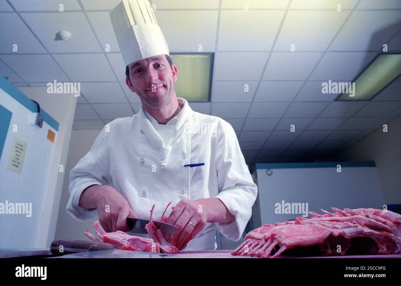 Ein Chefkoch mit traditionellem Haubenhut, der Fleischstücke in einer englischen Hotelküche zubereitet. Der Küchenchef ist Eddie Stevens, der zum Chefkoch im MoatHouse Hotel in Solihull ernannt wurde. Stockfoto