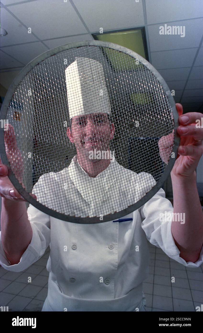 Eingerahmt von einem großen Sieb trägt dieser Küchenchef den traditionellen Haubenhut, nachdem er in einer englischen Hotelküche Fleischstücke zubereitet hat. Der Küchenchef ist Eddie Stevens, der zum Chefkoch im MoatHouse Hotel in Solihull ernannt wurde. Stockfoto