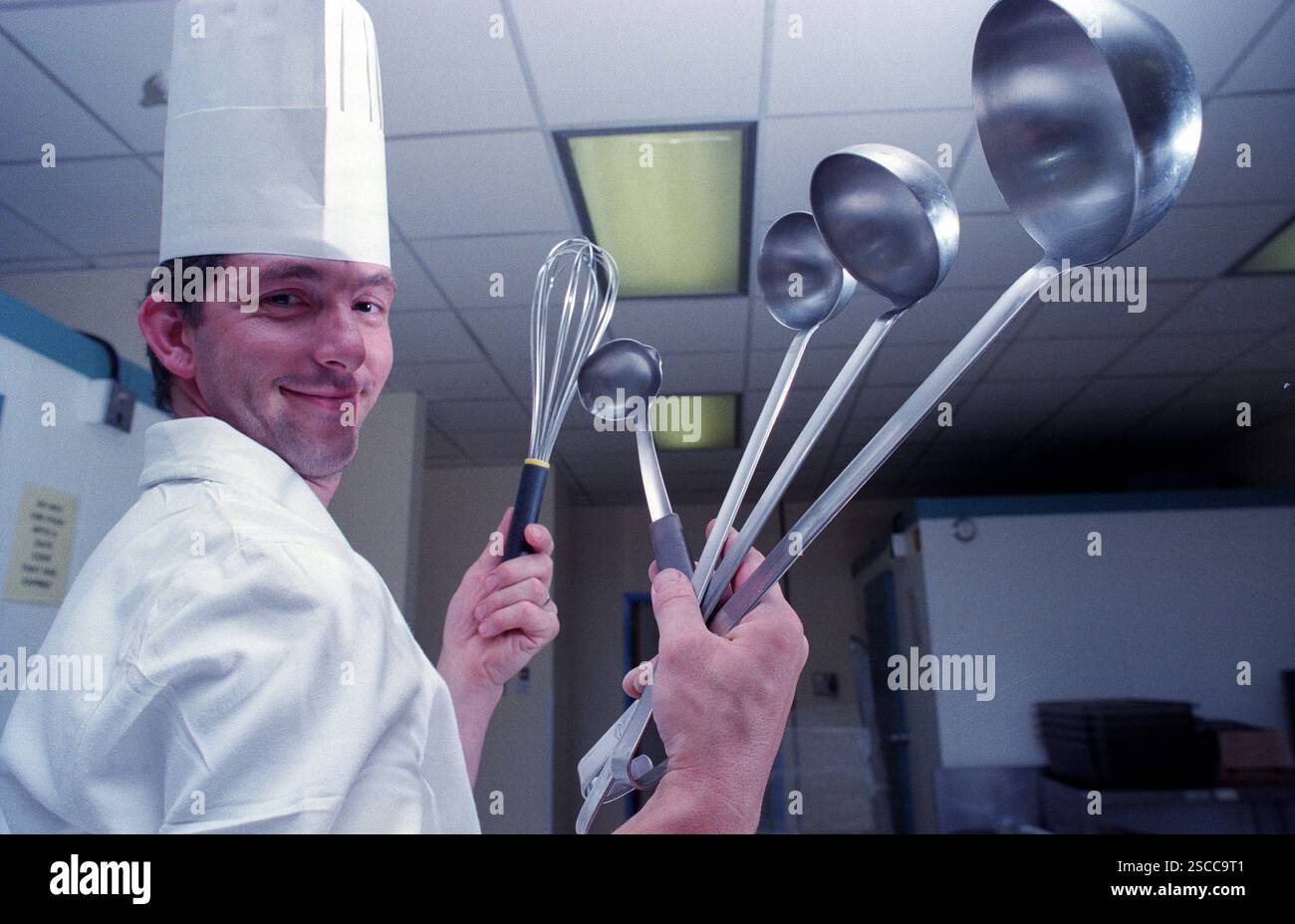 Mit einer Handvoll Küchenutensilien trägt der Chefkoch den traditionellen Haubenhut, nachdem er Fleischstücke in einer englischen Hotelküche zubereitet hat. Der Küchenchef ist Eddie Stevens, der zum Chefkoch im MoatHouse Hotel in Solihull ernannt wurde. Stockfoto