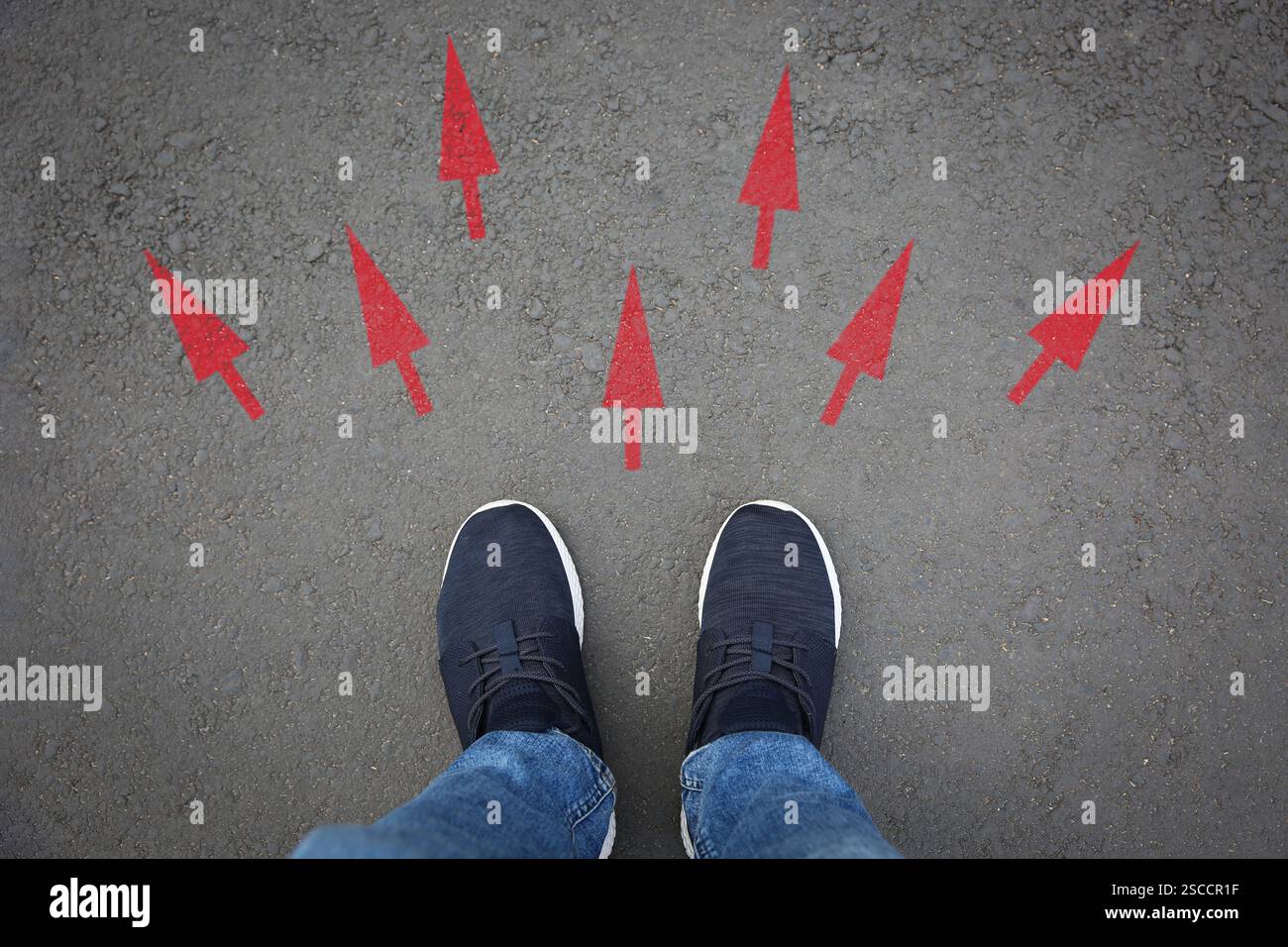 Mann, der neben roten Pfeilen auf Asphaltstraße steht, Nahaufnahme. Konzepte der Wahl, der Entscheidung, der anderen Art und Weise, der Alternative Stockfoto