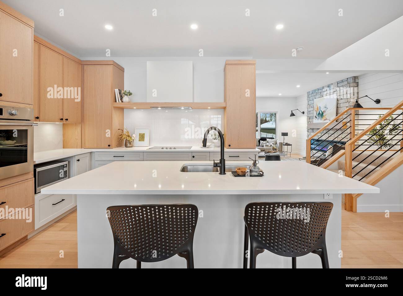 Eine Küche mit einer weißen Insel und zwei schwarzen Stühlen. Die Küche ist sauber und gut organisiert Stockfoto