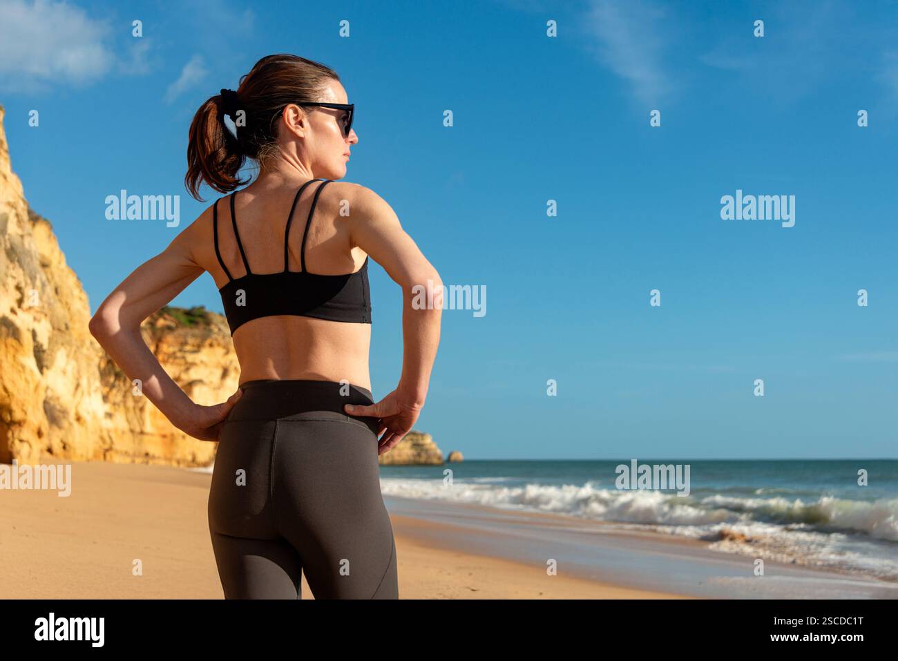 Sportliche Frau, die am Strand steht und die Hände auf den Hüften trägt und die Sonne genießt Stockfoto