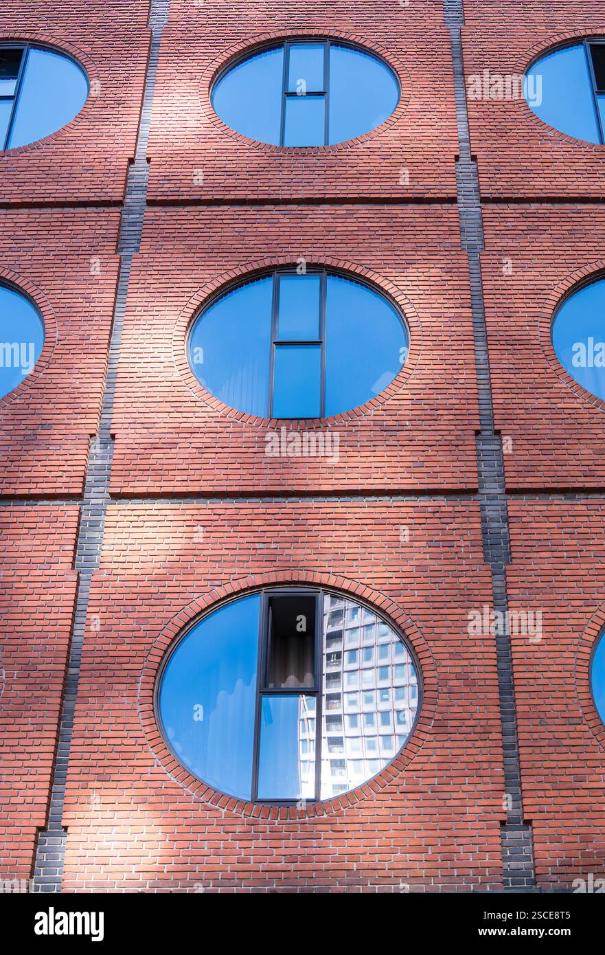 Eine moderne Ziegelwand verfügt über große, kreisförmige, blau getönte Fenster mit reflektierenden Scheiben. Stockfoto