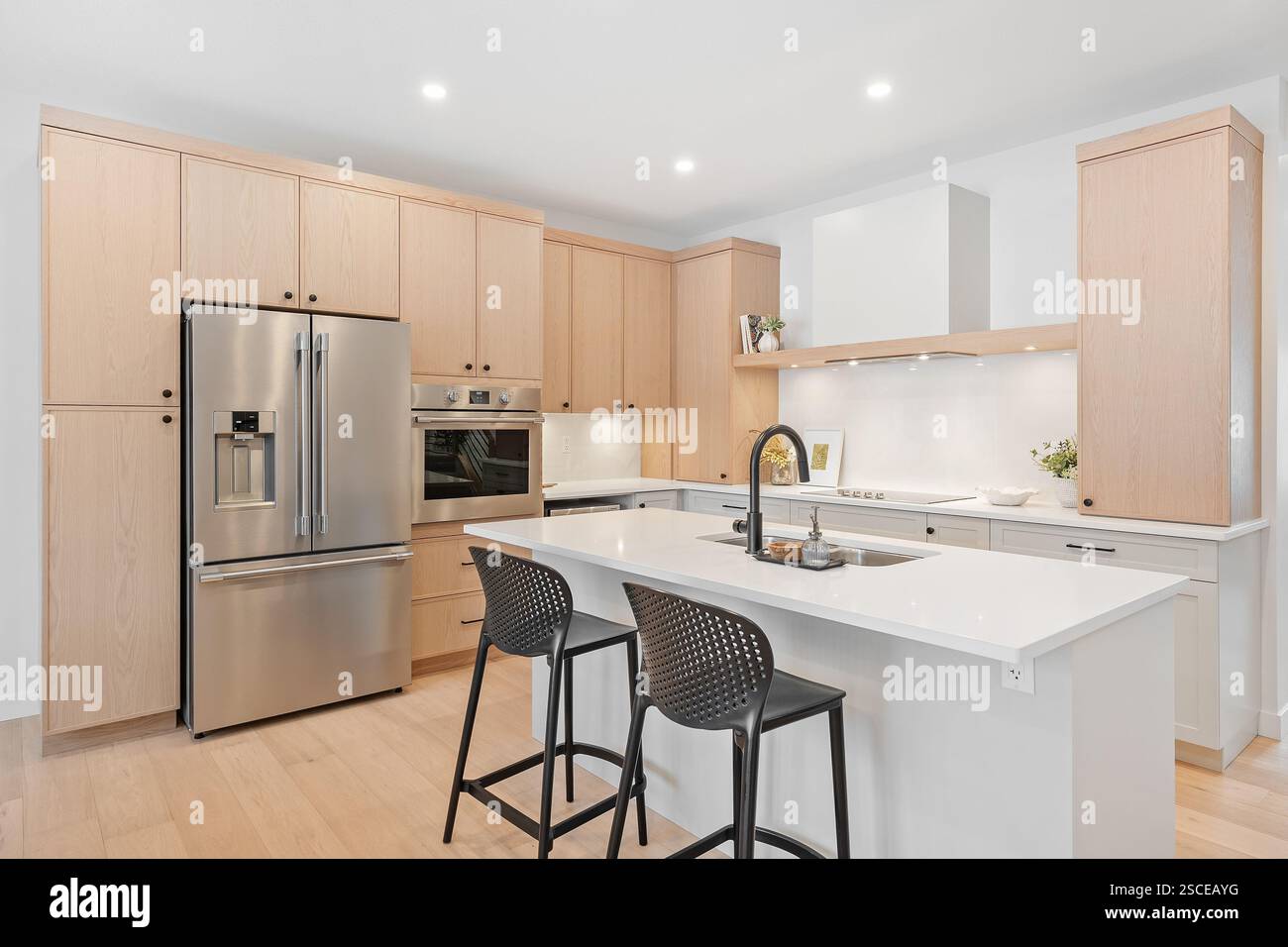 Eine Küche mit einer weißen Insel und zwei schwarzen Stühlen. Die Stühle stehen vor der Insel und es gibt ein Waschbecken und einen Kühlschrank im Zimmer. Stockfoto