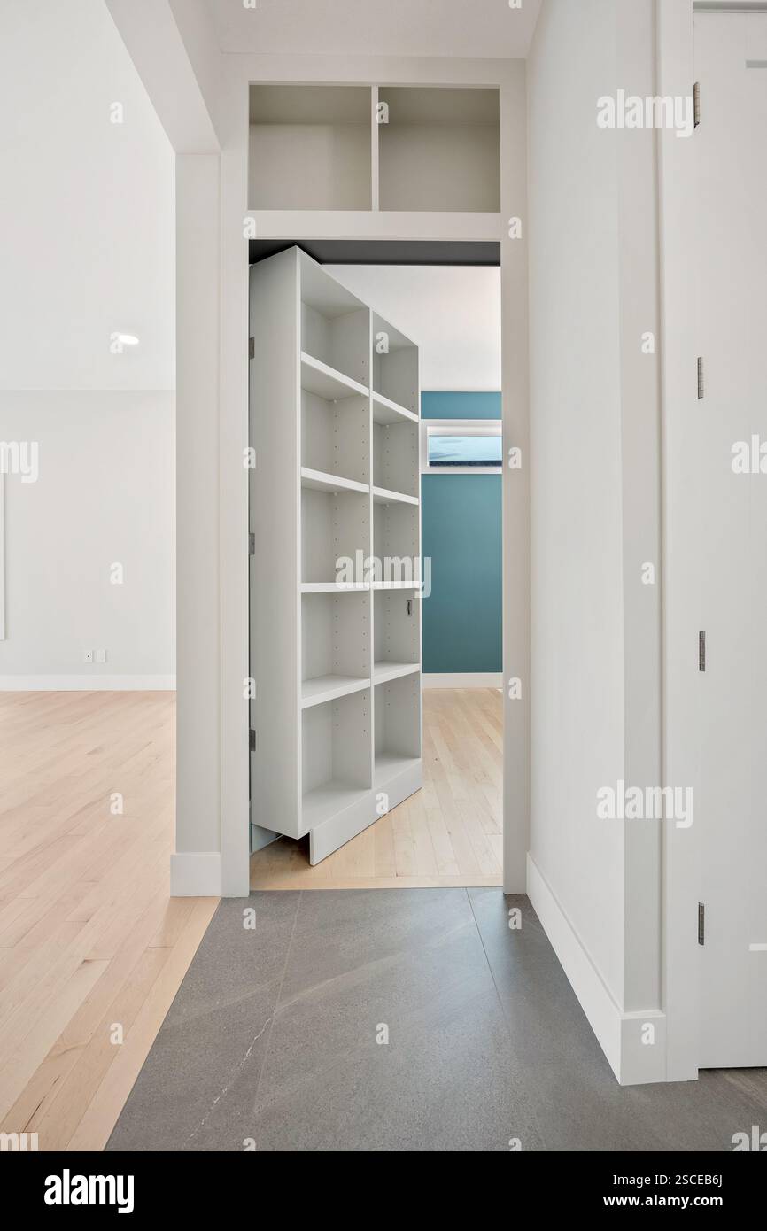 Ein weißes Zimmer mit einer blauen Wand und einer weißen Tür. Die Tür ist offen und zeigt einen weißen Schrank mit Regalen Stockfoto