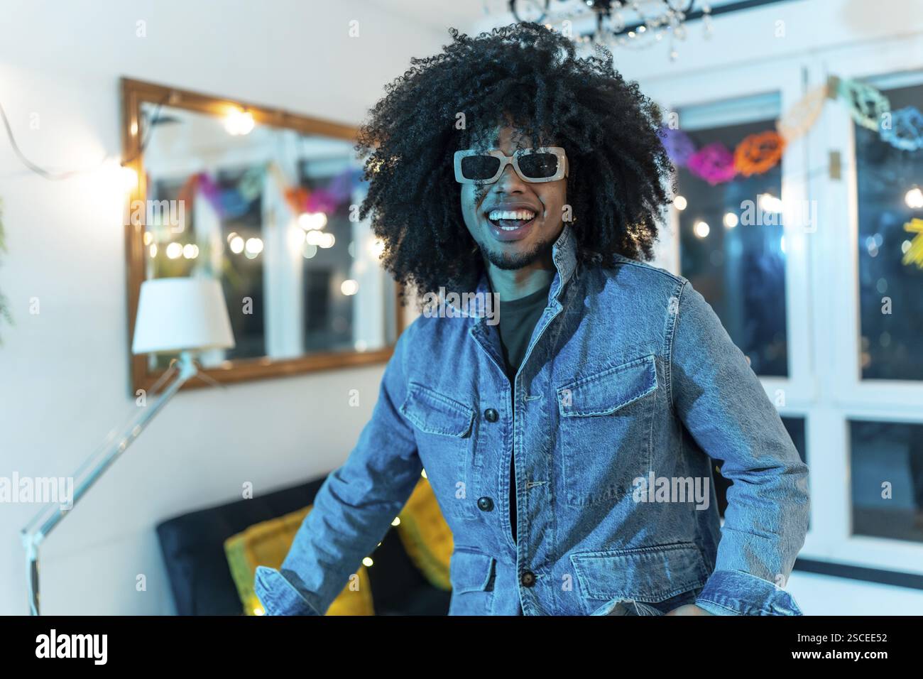 Porträt eines glücklichen jungen lateinmannes mit lockigen Haaren und Sonnenbrille, die auf einer Party zu Hause lächelt Stockfoto