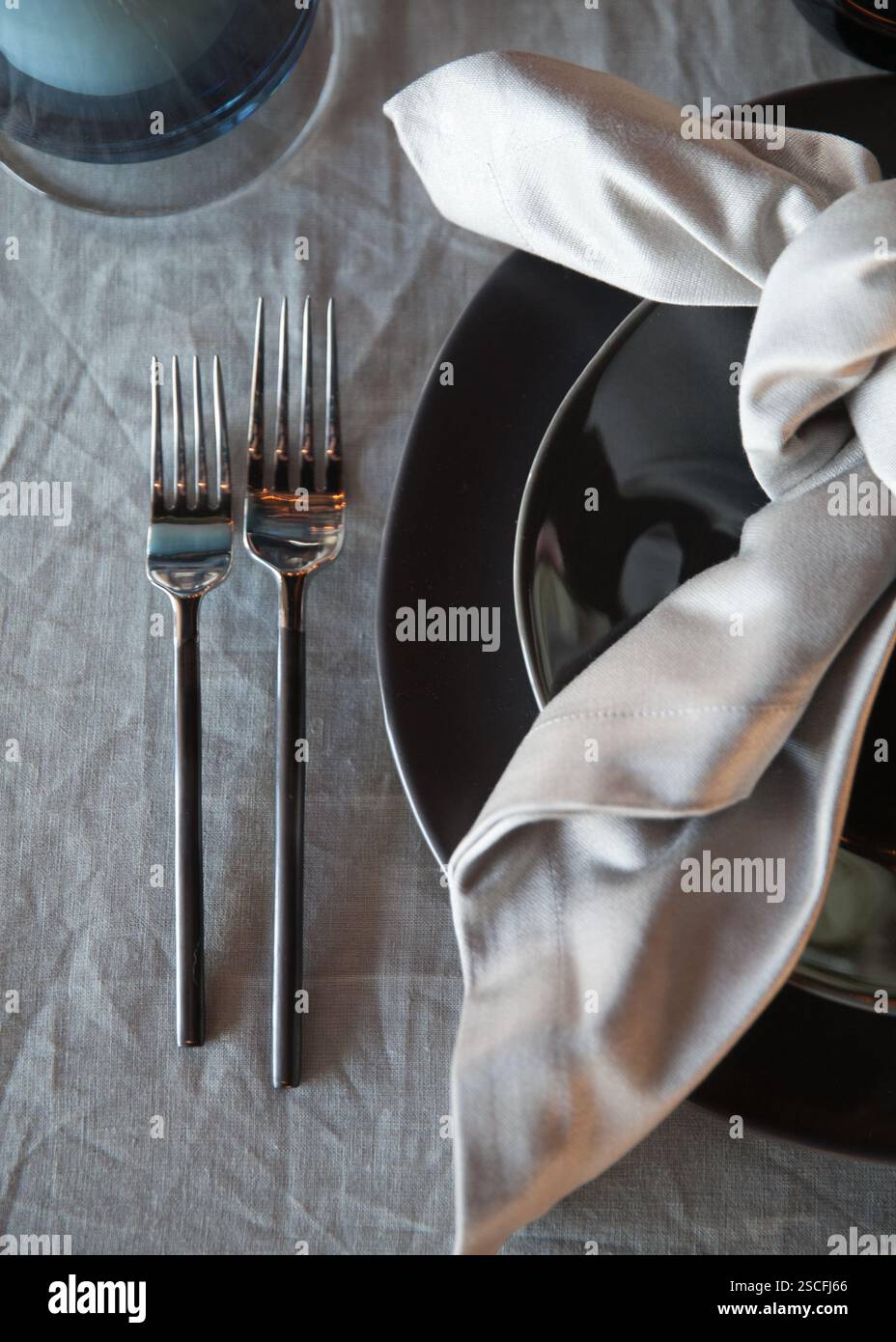 An einem wunderschön gestalteten Tisch finden Sie schwarzes Geschirr neben glänzenden Gabeln und einer ordentlich platzierten Stoffserviette. Die elegante Einrichtung lädt zum Abendessen ein Stockfoto