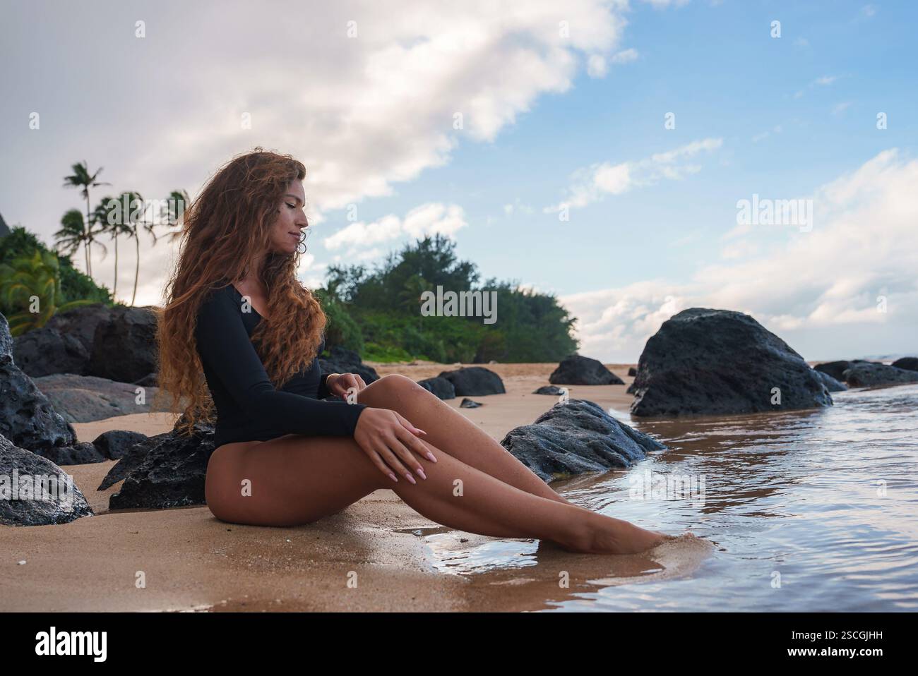 Frau, die am Tropical Beach mit vulkanischen Felsen und Palmen sitzt Stockfoto