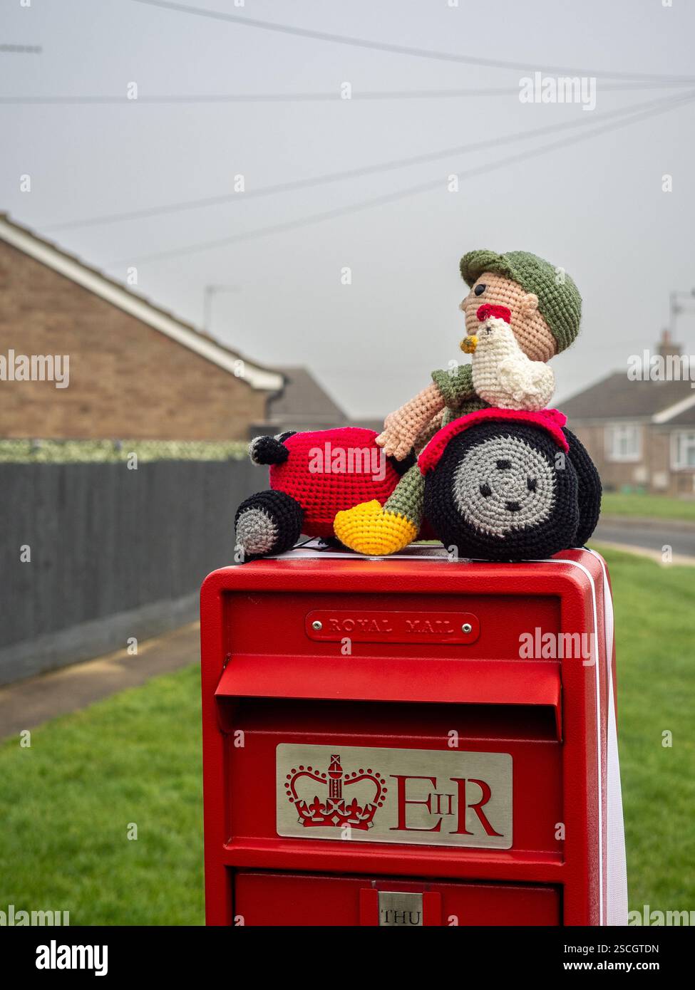 Royal Mail Postbox mit gestricktem Topper mit einem Bauern mit einem Huhn auf einem Traktor, Hackleton, Northamptonshire, Großbritannien Stockfoto