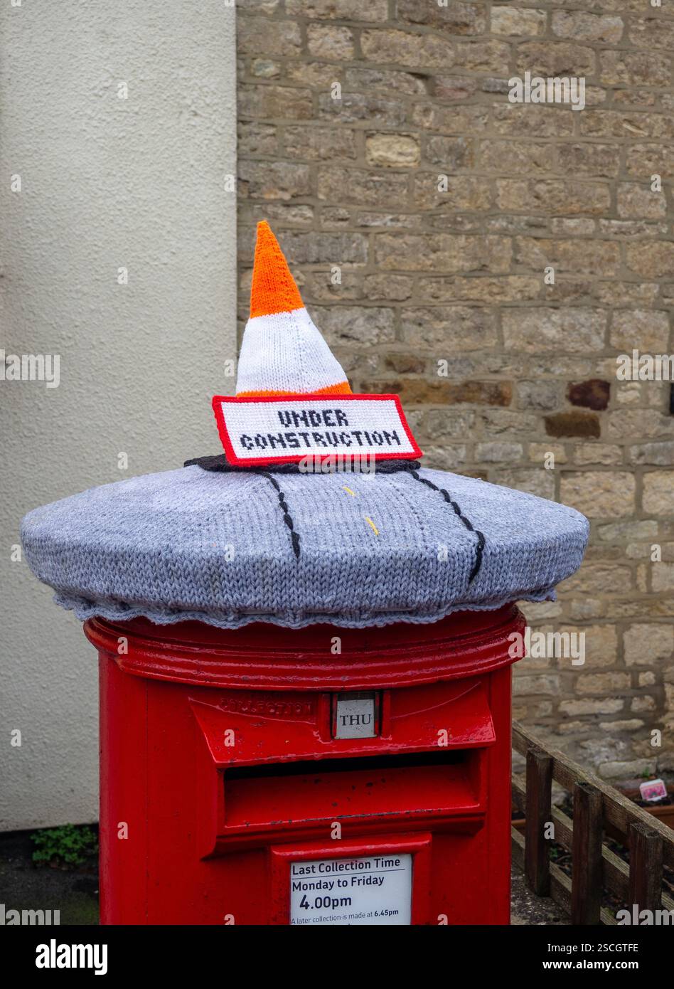 Royal Mail Postbox mit gestricktem Oberteil mit einem Verkehrskegel und einem Schild unter dem Bau, Hackleton, Northamptonshire, Großbritannien Stockfoto