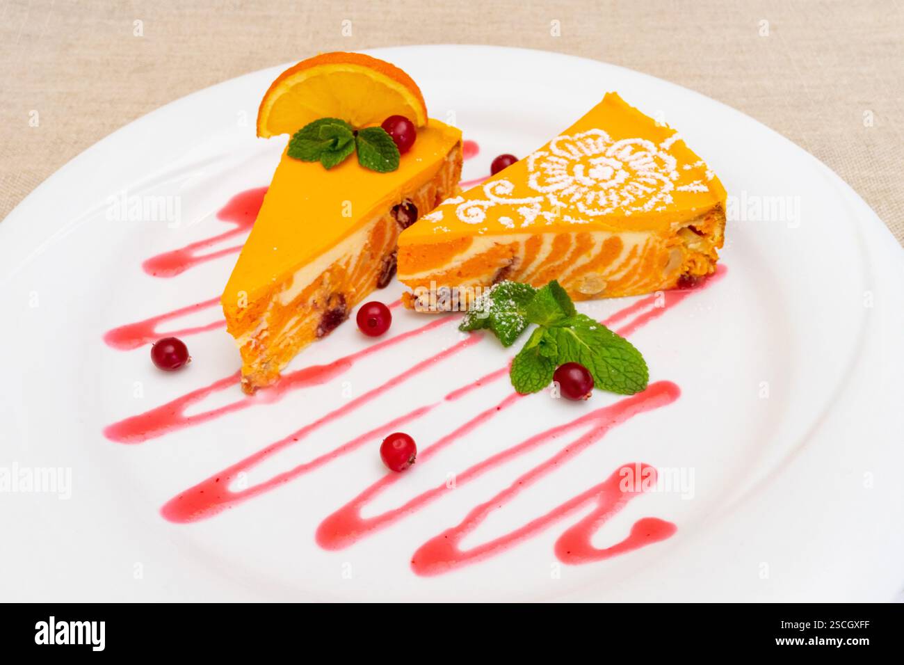 Zwei Stück lebendiges Orangendessert auf einem weißen Teller, garniert mit Minzblättern und Himbeersauce. Das süße Leckerli enthält eine pikante Zitrusfrucht Stockfoto