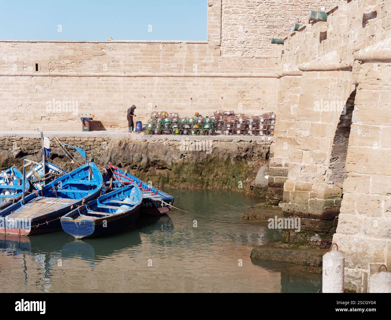 Der Mensch fischt in Essaouira, Marokko, im Februar 2025 mit blauen Booten und Bogengängen neben der Stadtmauer Stockfoto
