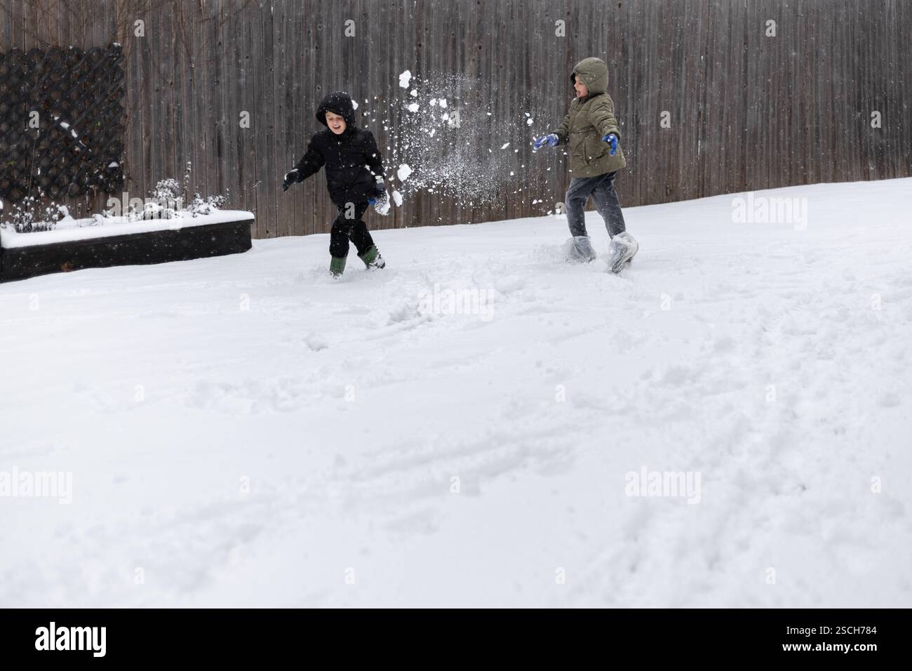 Zwei Kinder werfen Schneebälle und rennen in einem Garten Stockfoto