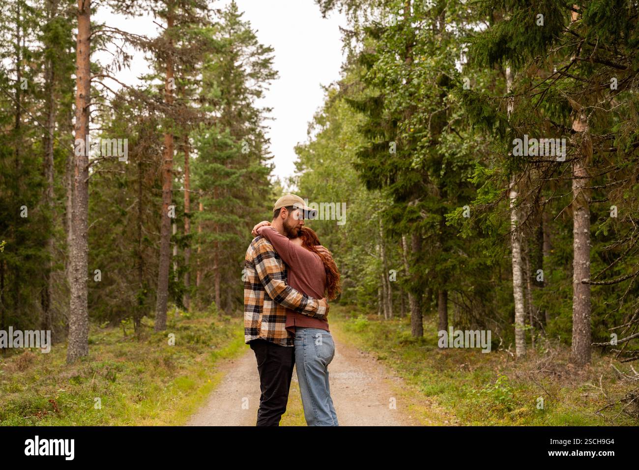 Ein Paar umgibt sich auf einem malerischen Pfad, umgeben von üppigen grünen Bäumen in einem ruhigen schwedischen Wald. Ein friedlicher Moment der Verbindung mit der Natur in einer Ruhe Stockfoto