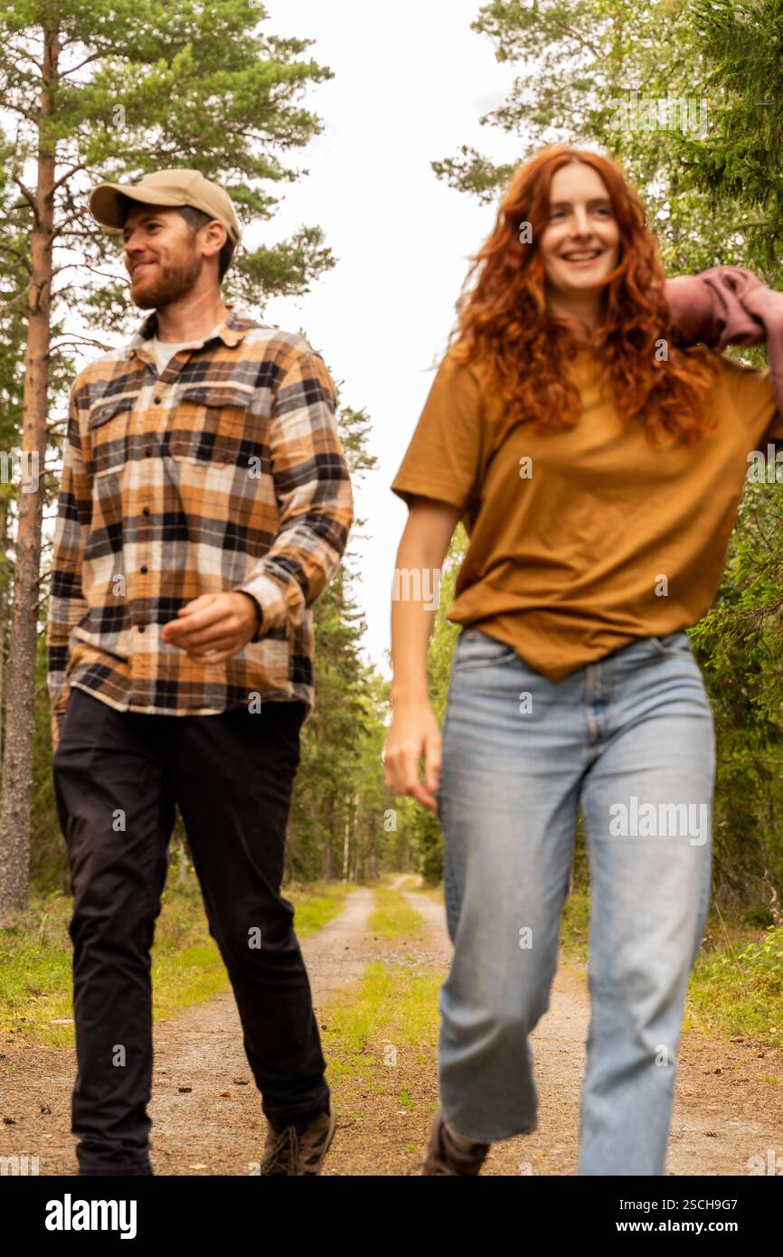 Ein paar spazieren fröhlich durch einen üppigen Waldweg in Schweden. Sie tragen legere Kleidung, genießen die Natur und genießen eine friedliche Wanderung zwischen hohen Kiefern Stockfoto