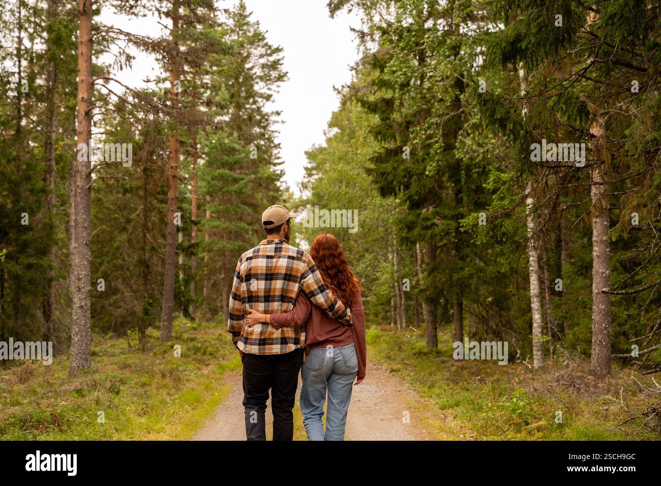 Ein Paar umarmt sich auf einem üppig grünen Waldweg in Schweden, umgeben von hohen Bäumen und natürlicher Schönheit, die Liebe und Ruhe symbolisieren Stockfoto