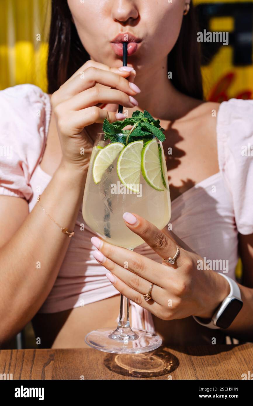 Eine Person genießt ein erfrischendes Limettengetränk mit Minze und Eis, perfekt für Grillpartys im Freien. Die Umgebung ist hell und sommerlich, was eine entspannte und entspannte Atmosphäre schafft Stockfoto