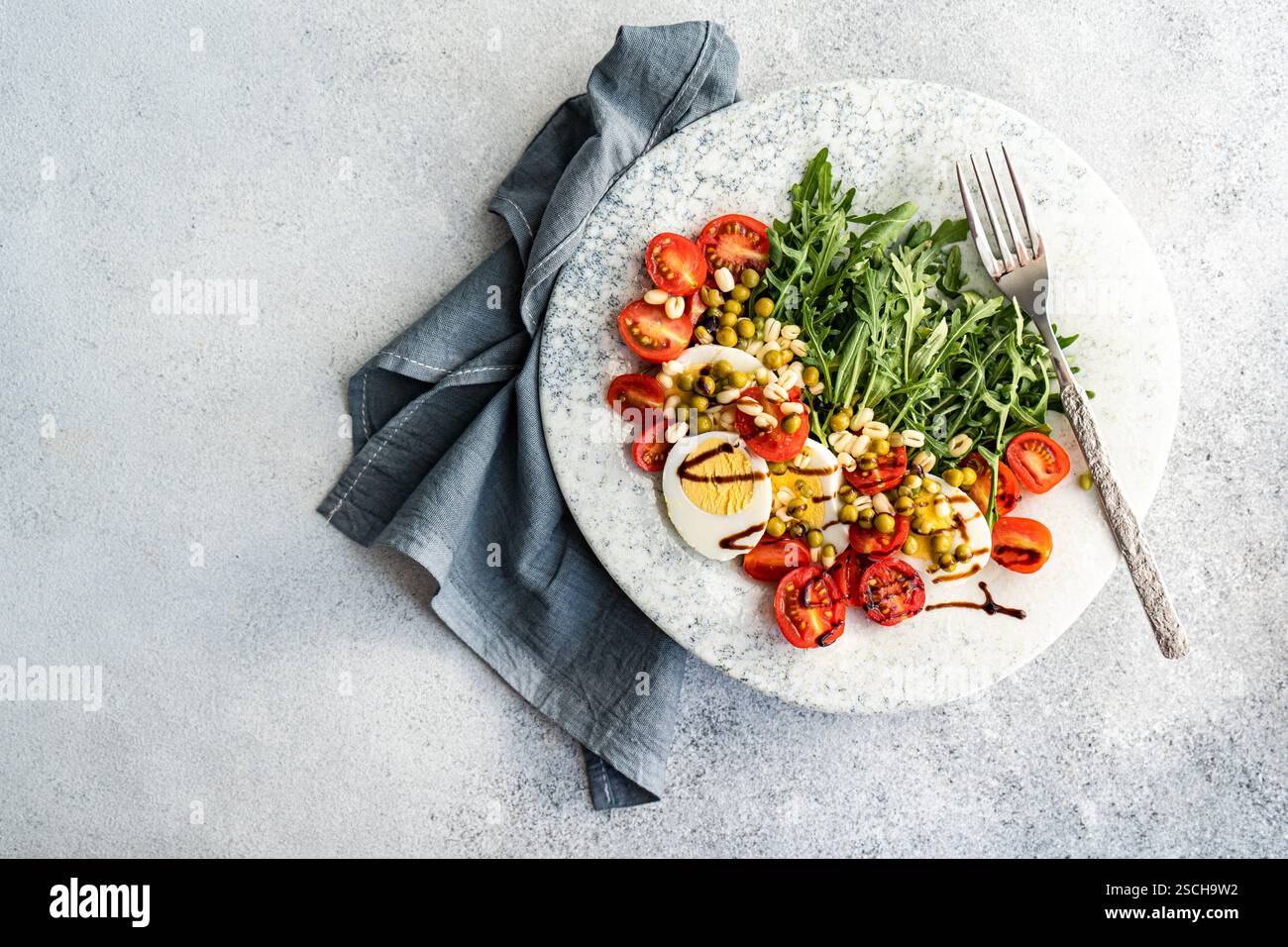 Köstliche Keto-Mahlzeit mit gekochten Eiern, frischer Rakete, Kirschtomaten, grünen Erbsen und gekeimten Bohnen, elegant serviert mit Balsamico-Soße für eine Stockfoto