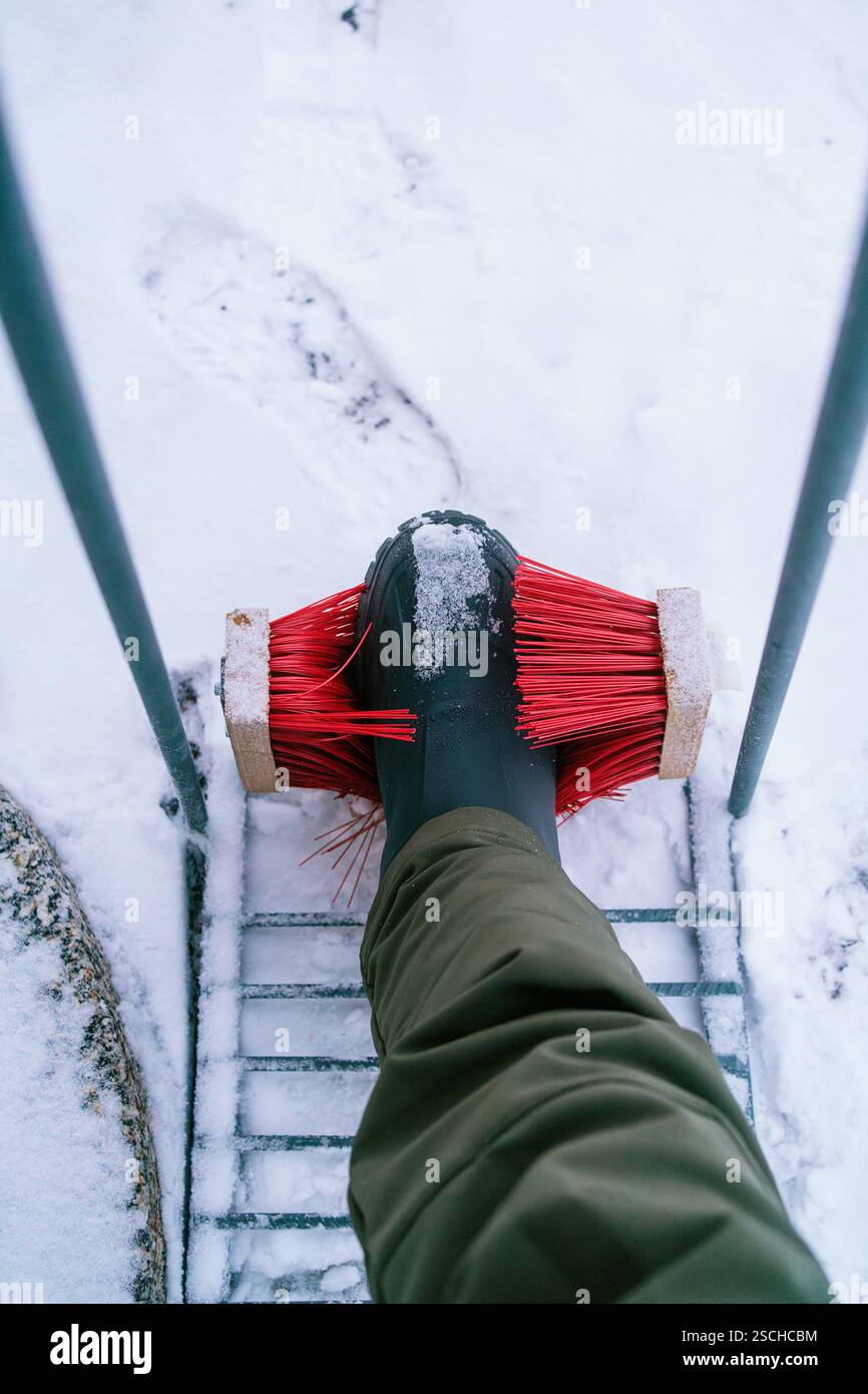 Eine Person reinigt den Schnee mit einer roten Bürste vor einem verschneiten Hintergrund in Schwedisch Lappland. Das praktische Winterwerkzeug sorgt für Sauberkeit Stockfoto