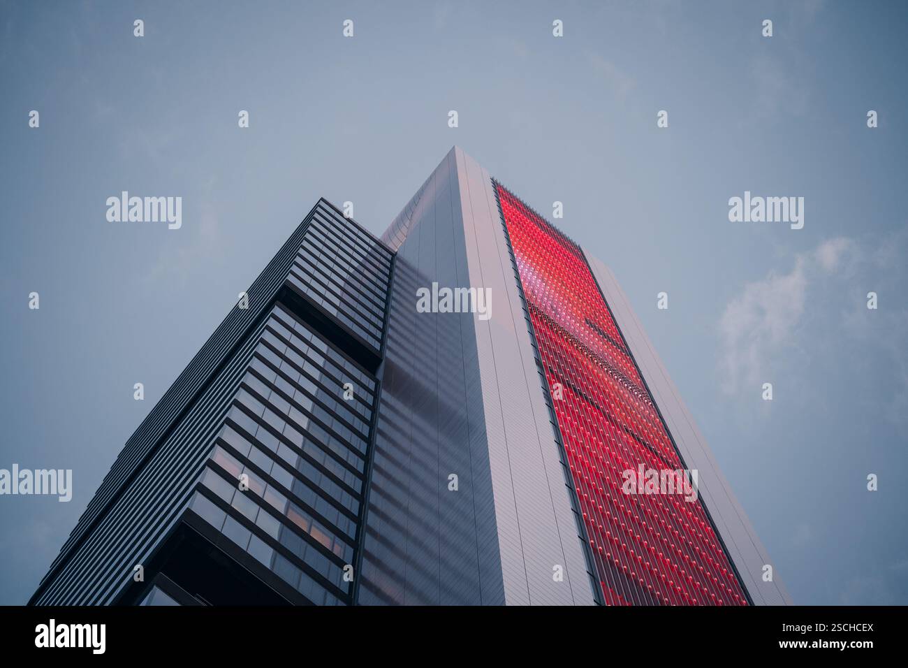 Flacher Blick auf einen modernen Wolkenkratzer mit markanter roter Fassade vor klarem Himmel. Die schlanke Architektur verkörpert urbane Raffinesse und City li Stockfoto