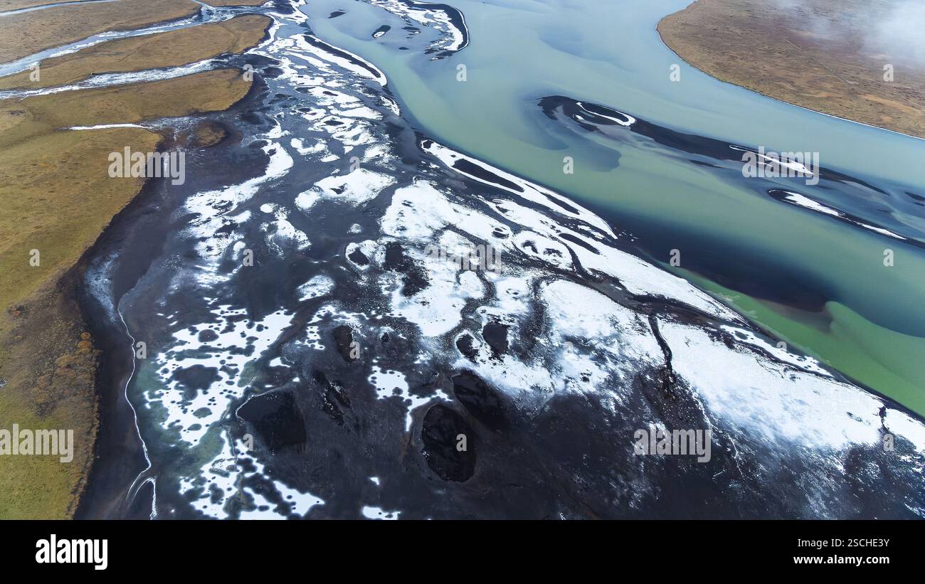 Atemberaubendes Luftdrohnenbild, das Islands Flüsse einfängt, die sich durch schneebedeckte Landschaften in der Nähe der Küste schlängeln und Kontraste von eisblauem Wasser zeigt Stockfoto
