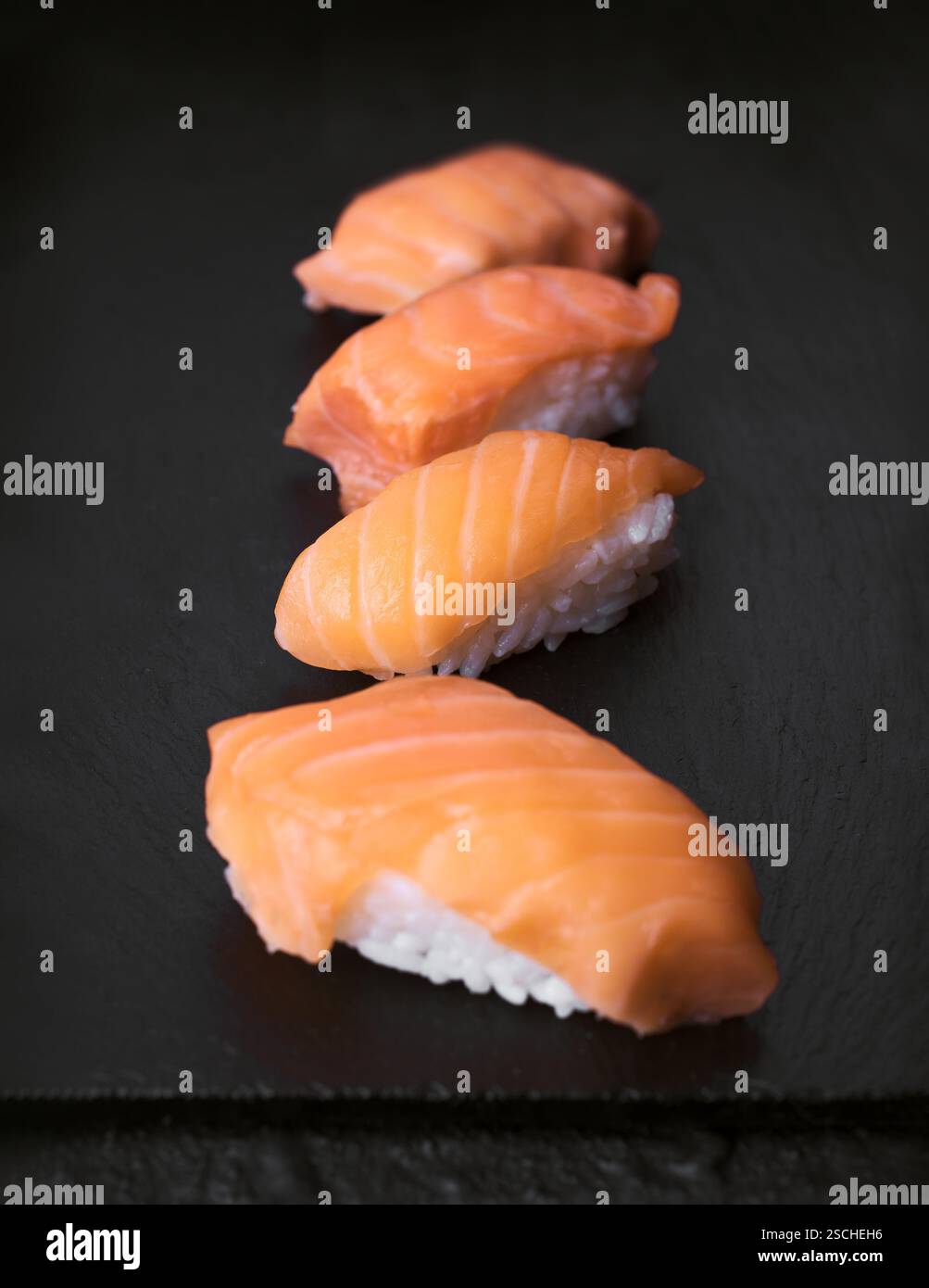 Eine Auswahl an Sushi-Stücken mit Lachs, elegant auf einer schwarzen Steinoberfläche. Perfekt für die Illustration authentischer japanischer Küche und Cu Stockfoto