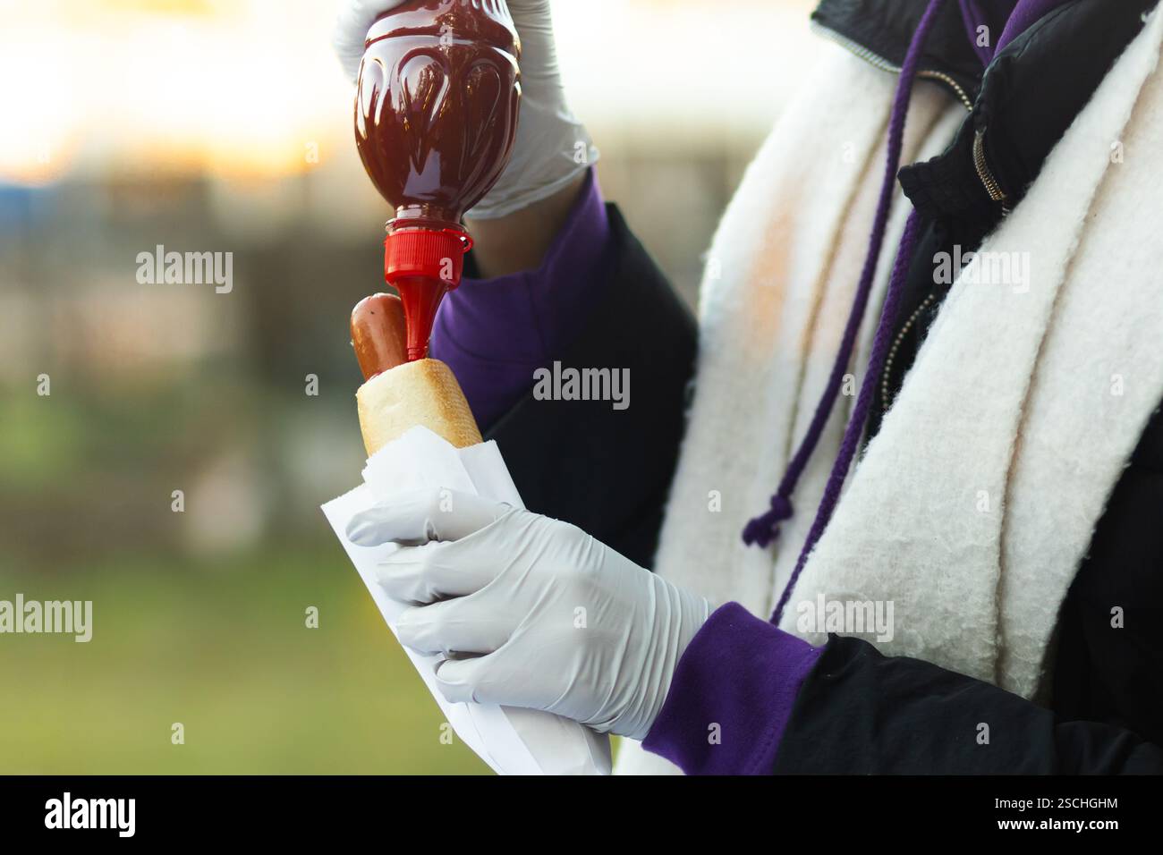 Zugeschnittenes, nicht erkennbares Foto einer Person, die auf einer Messe im Freien einen Hot Dog mit Sauce serviert. Der Schwerpunkt liegt auf dem Prozess der Lebensmittelzubereitung, hochlig Stockfoto