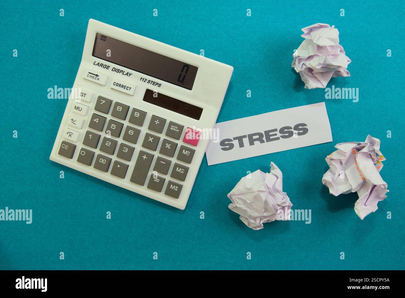 Ein großer Taschenrechner befindet sich neben zerknitterten Papieren, die mit Stress gekennzeichnet sind, und zeigt den Druck von Büroaufgaben an. Stockfoto