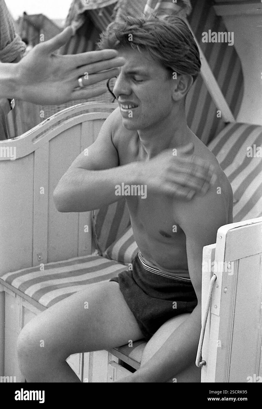 Ein junger Mann in Badehose sitzt in einem Liegestuhl vor dem Pier in Ahlbeck an der Ostsee. [Automatisierte Übersetzung] Stockfoto
