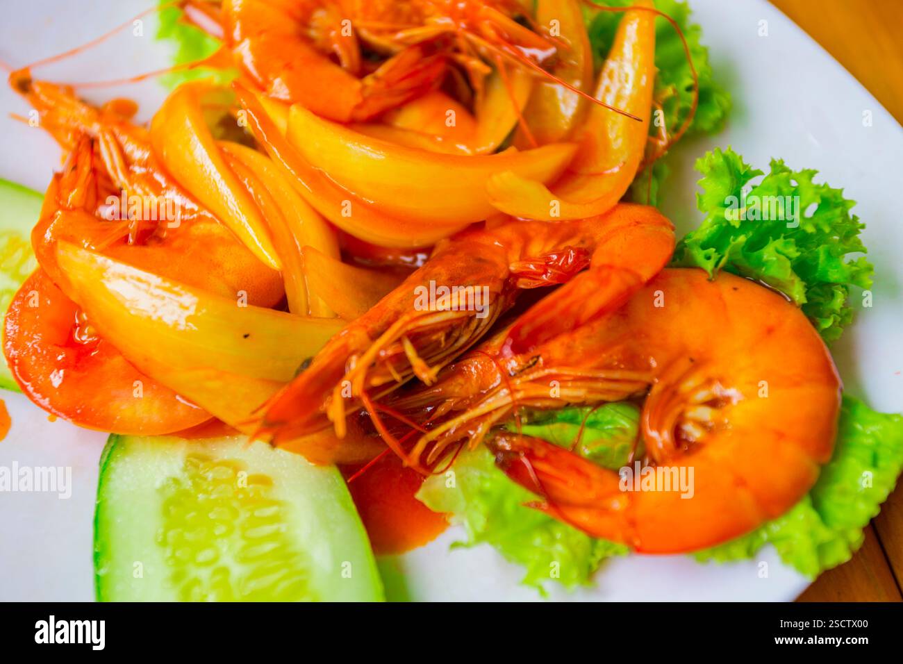 Garnelen mit Zwiebeln, Salat, Gurke und Sauersauce auf einem weißen Teller Stockfoto